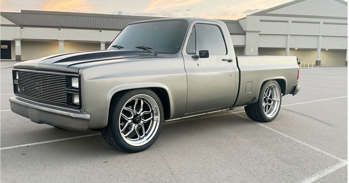 Silver Chevy pickup truck with black hood, parked on concrete.
