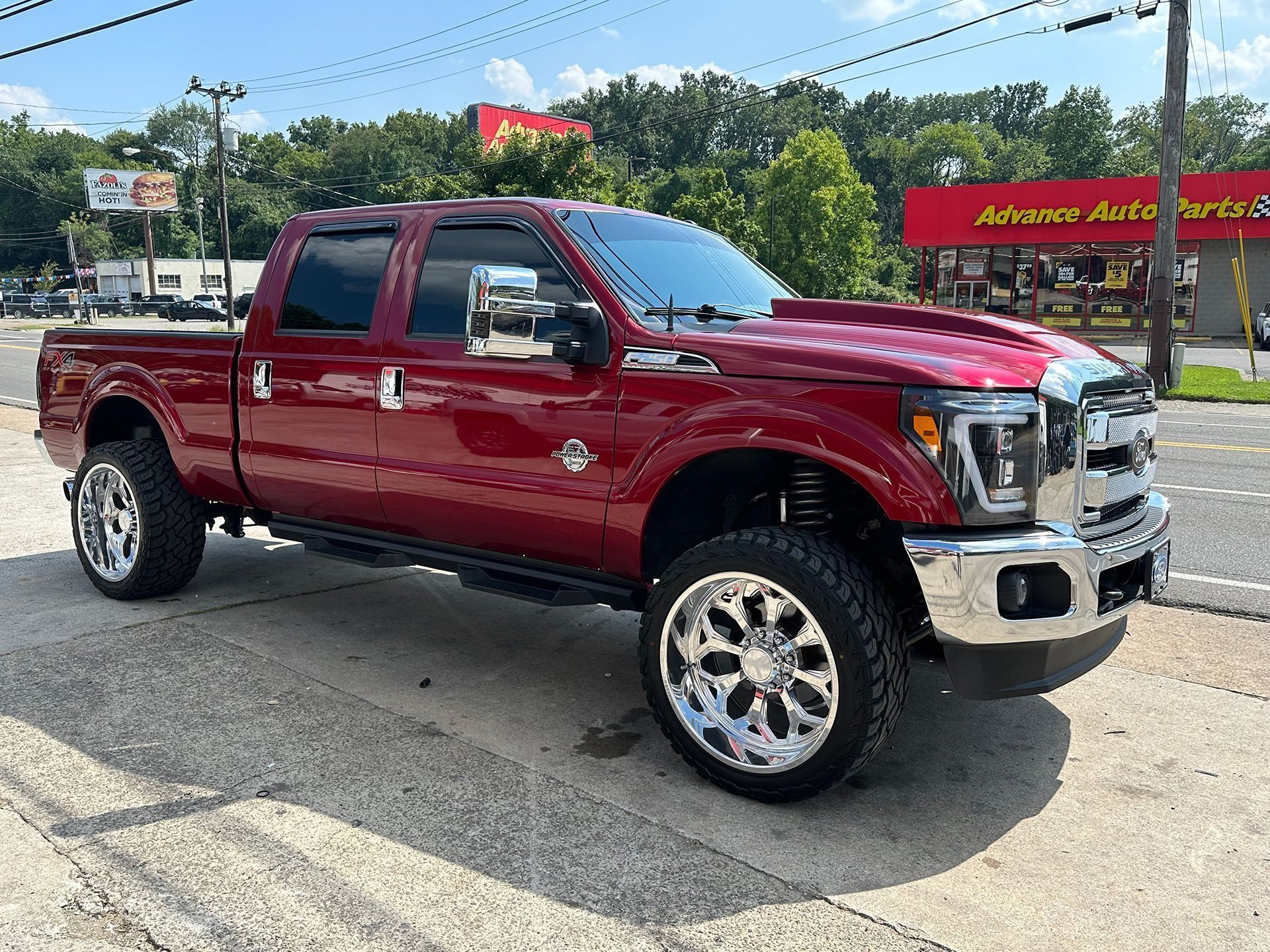 Red pickup truck parked near an Advance Auto Parts store on a sunny day. Chrome wheels.