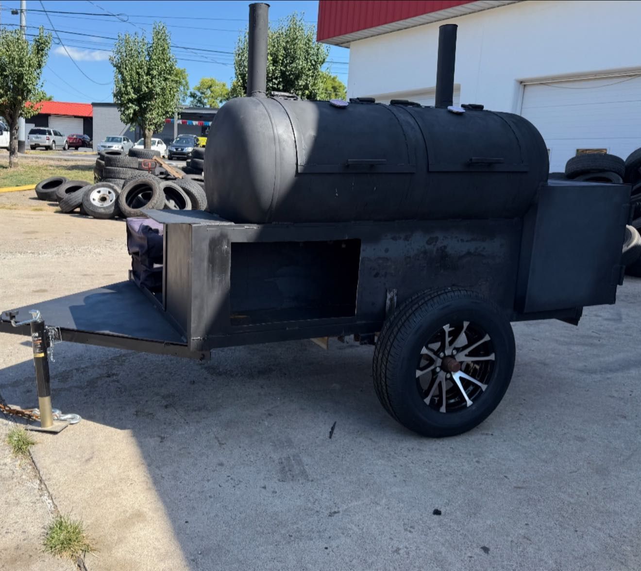 Black smoker on a trailer; outdoors near a building and tires.