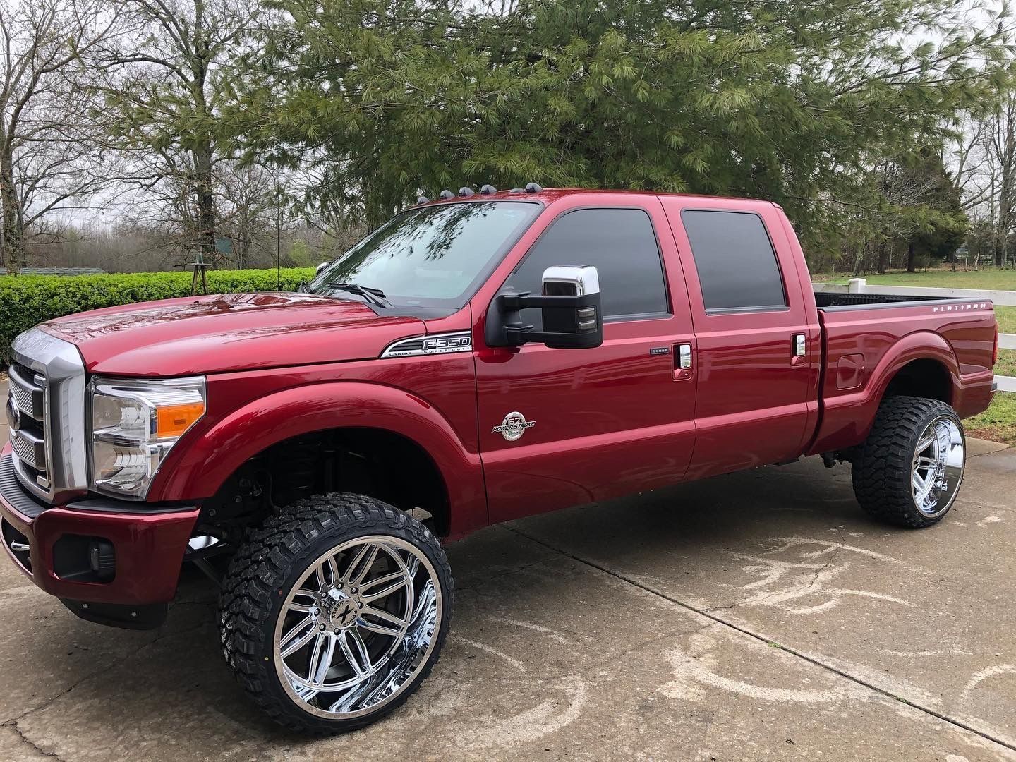 Red lifted pickup truck with chrome wheels parked on a driveway.