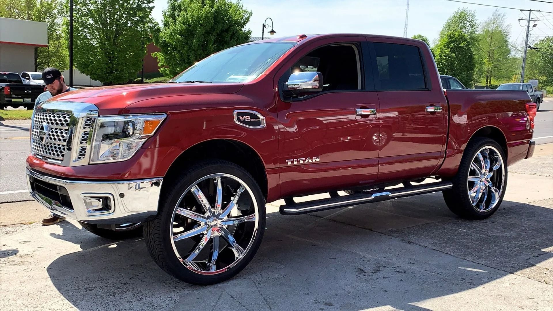 Red Nissan Titan truck with chrome wheels and running boards parked outside.