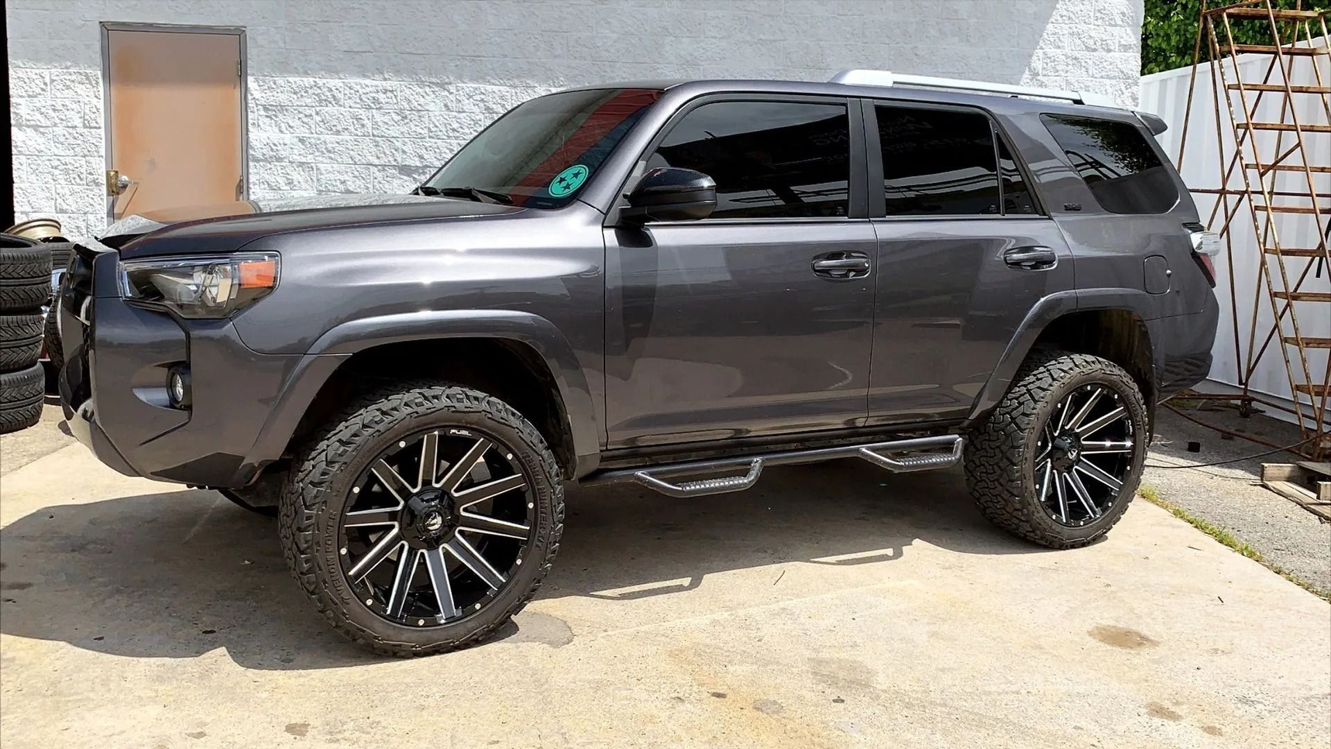 Gray SUV with black wheels parked on a paved surface next to a building.