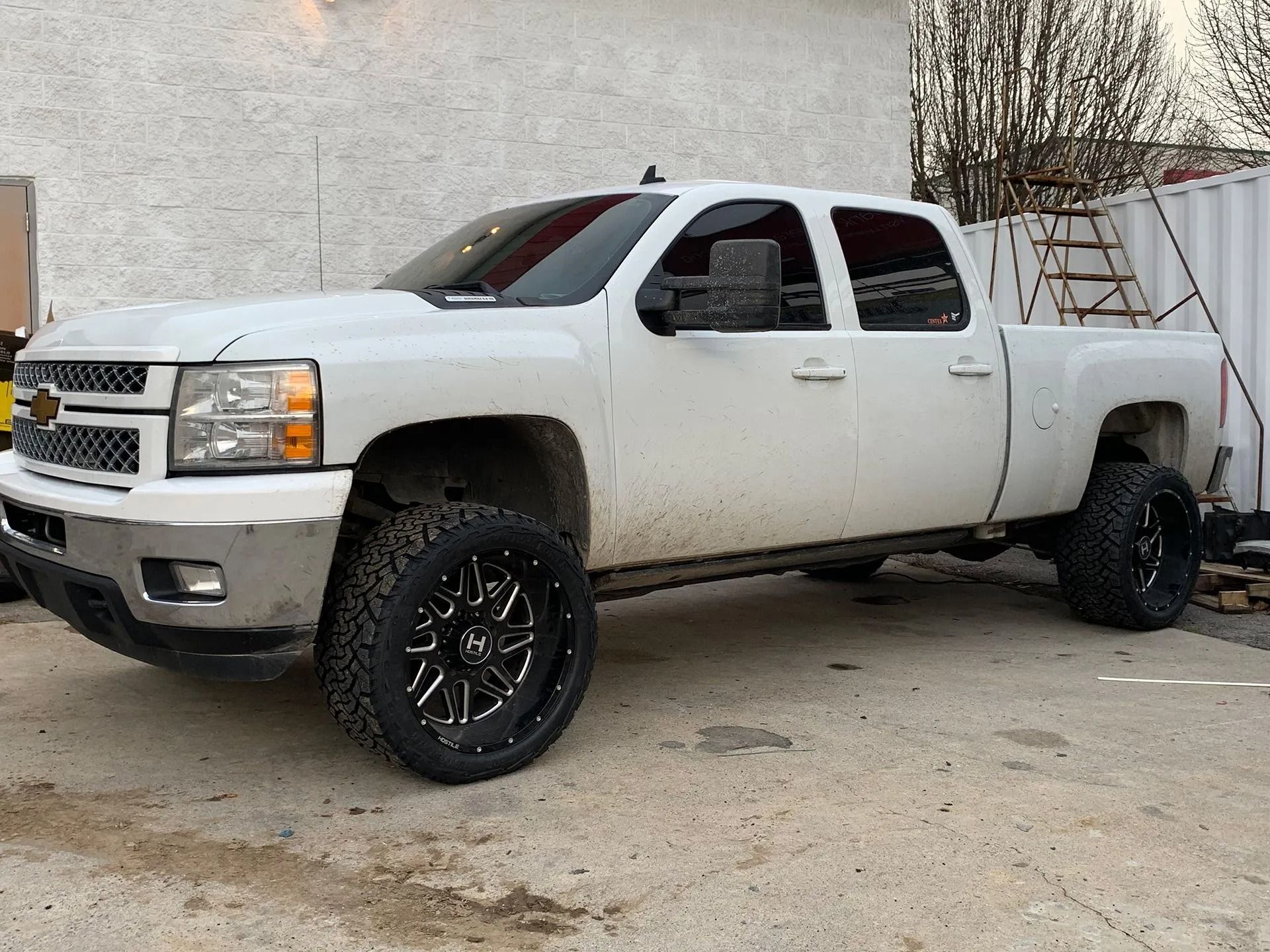 White Chevy truck parked, black wheels, dirty sides, setting near a building.