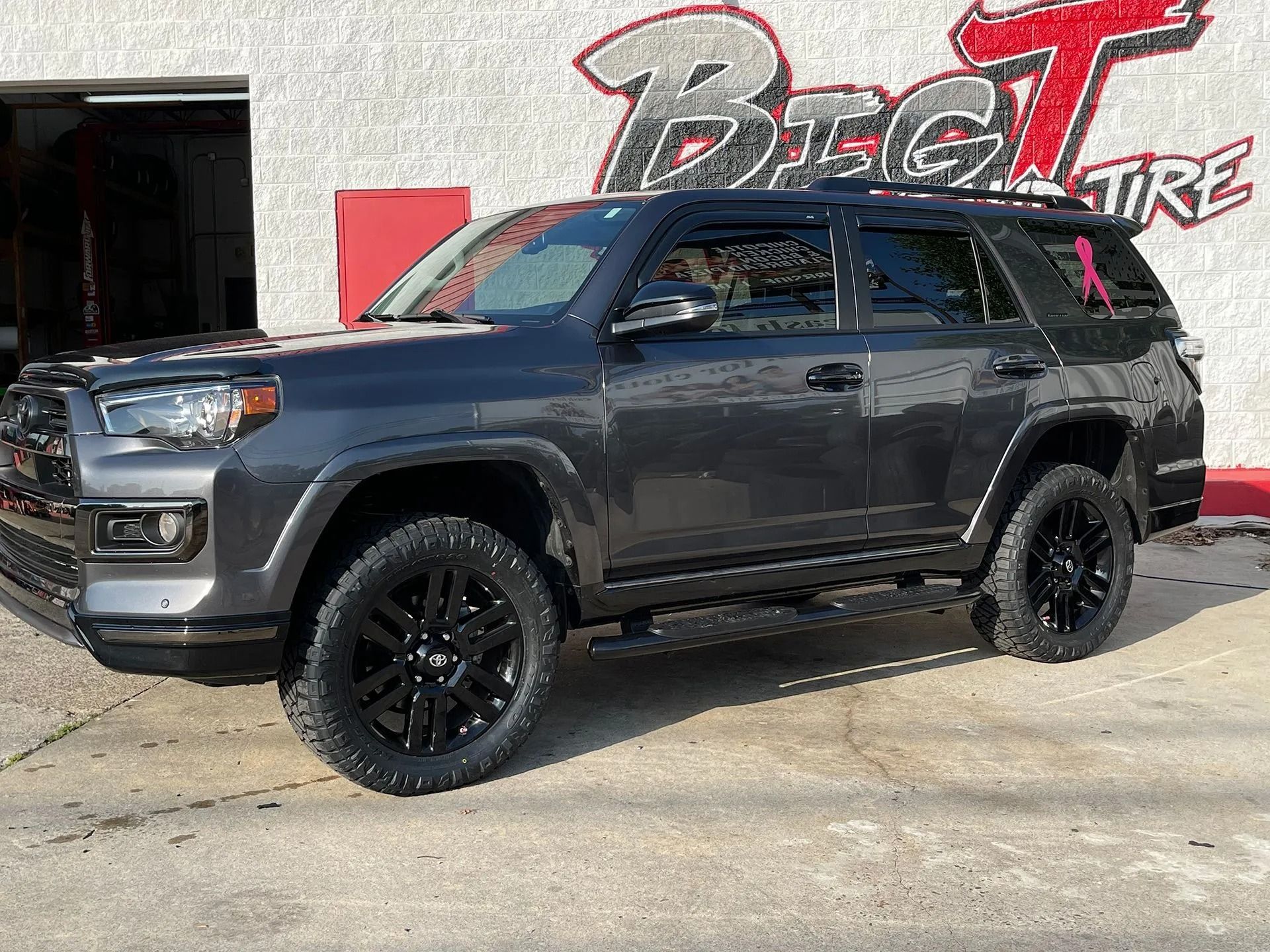 Dark gray Toyota 4Runner with black wheels parked outside a tire shop.