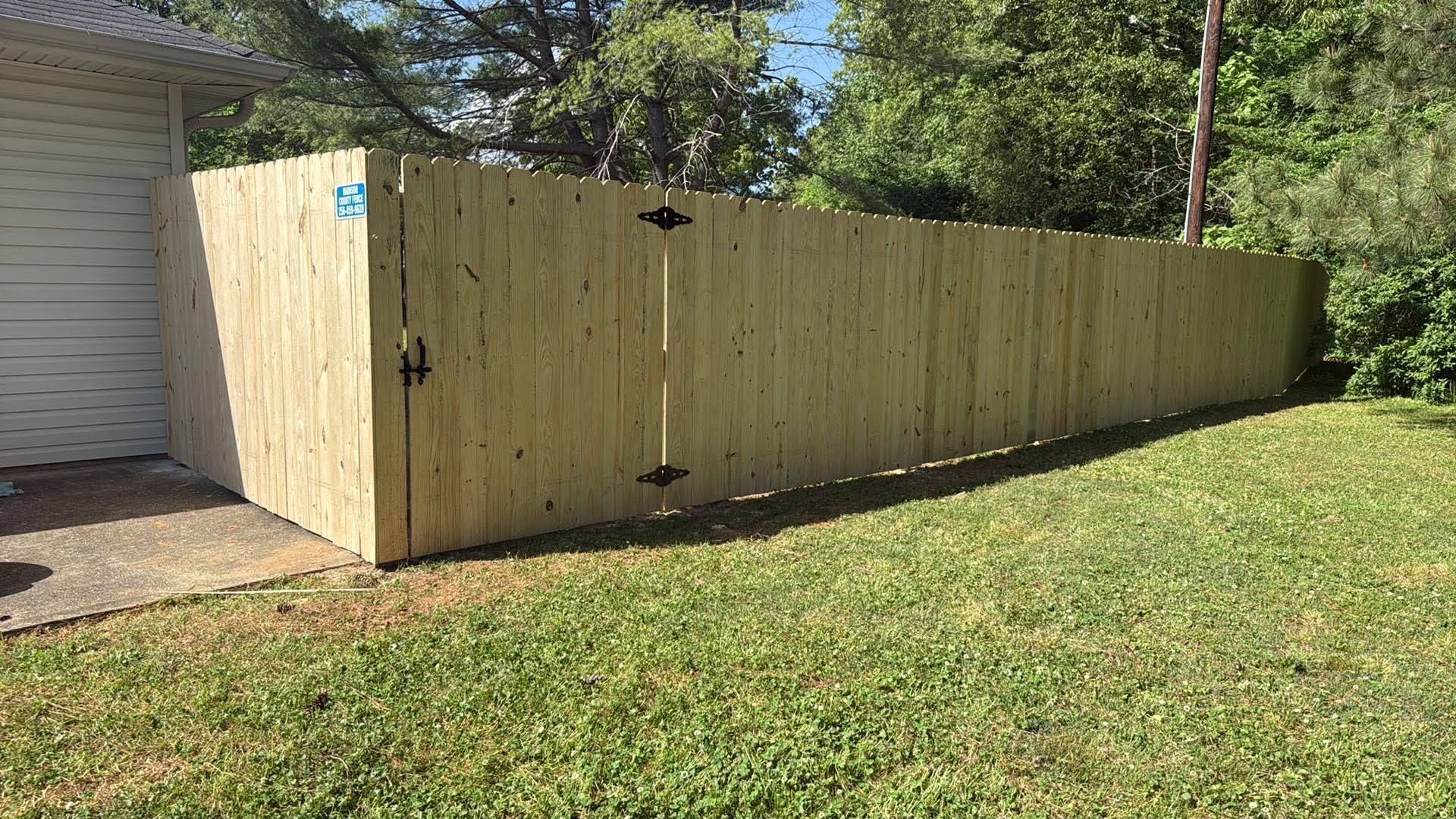 Wooden privacy fence along a grassy yard beside a garage, lit by bright sunlight.