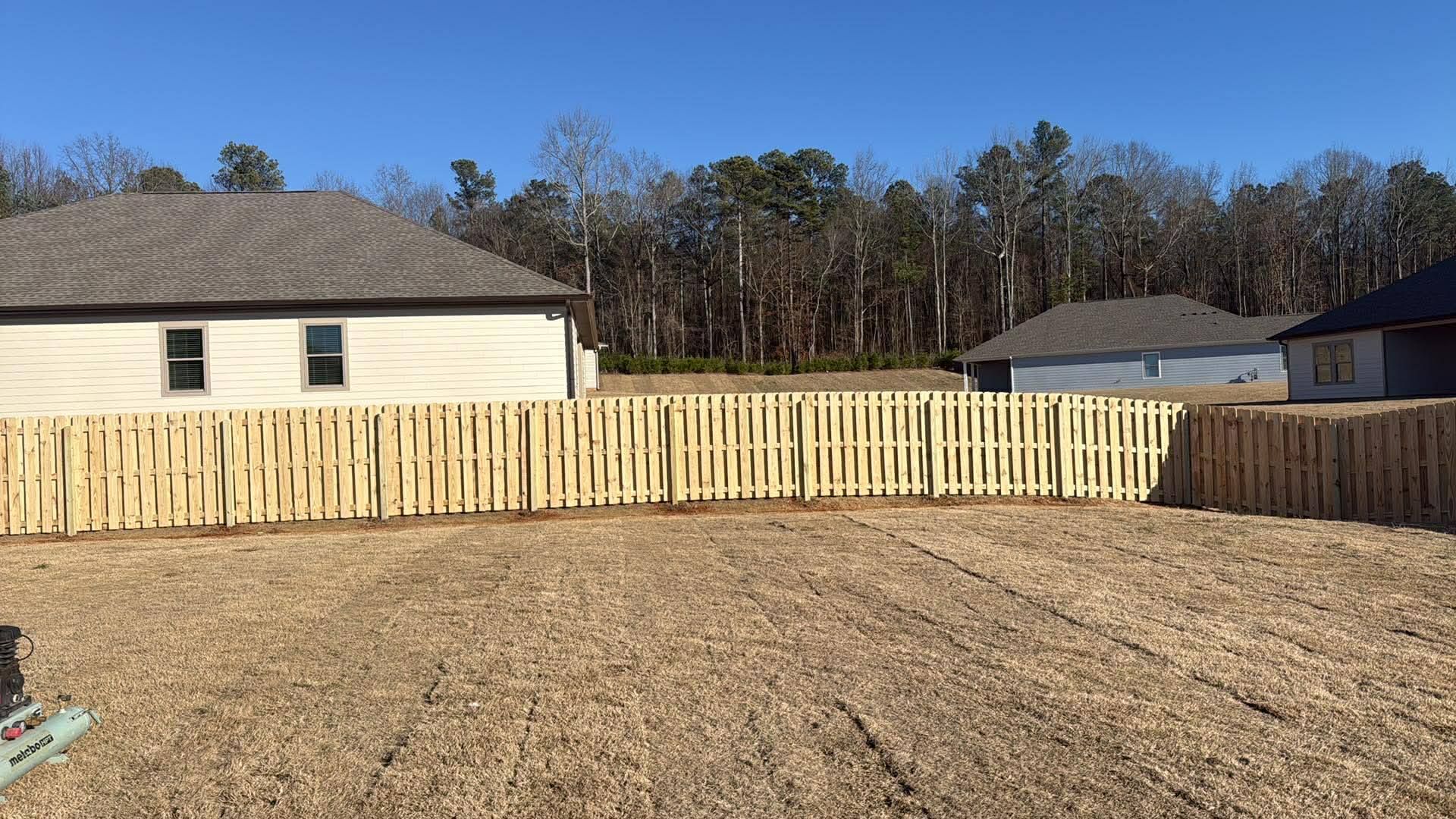 Backyard with fresh wooden privacy fence and bare lawn under clear blue sky.