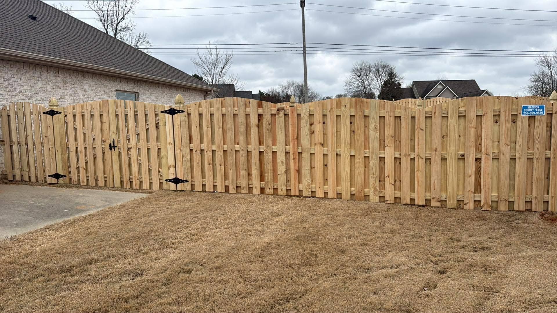 Wooden privacy fence along a suburban backyard beside a house and driveway under a cloudy sky.