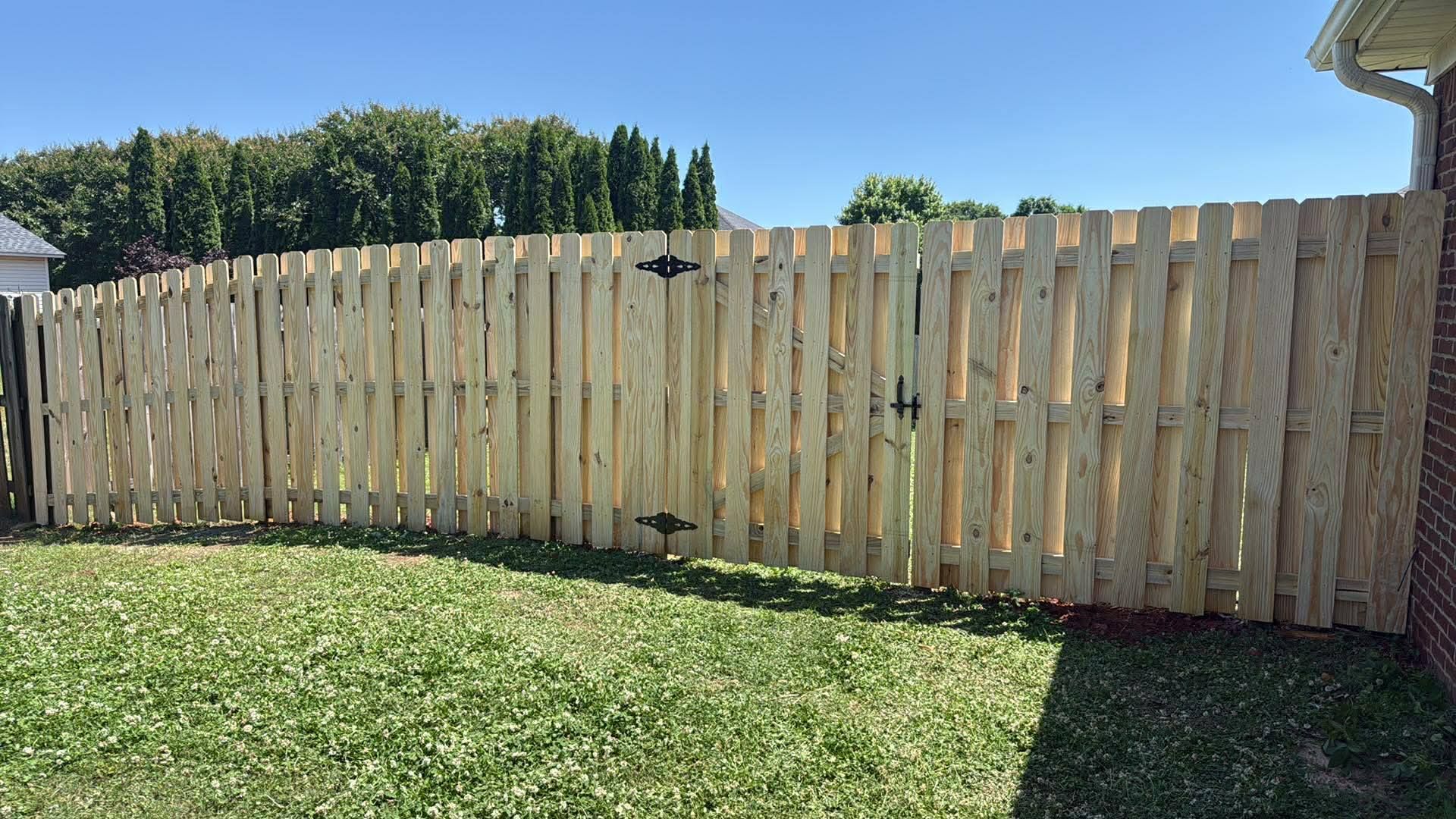 Wooden backyard fence with a grassy lawn under a clear blue sky.