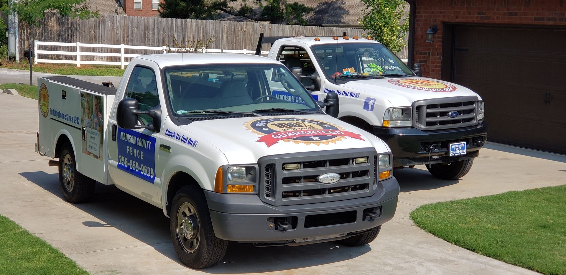 Two white service trucks parked on a driveway. One truck has a tool box. Both trucks have company logos.