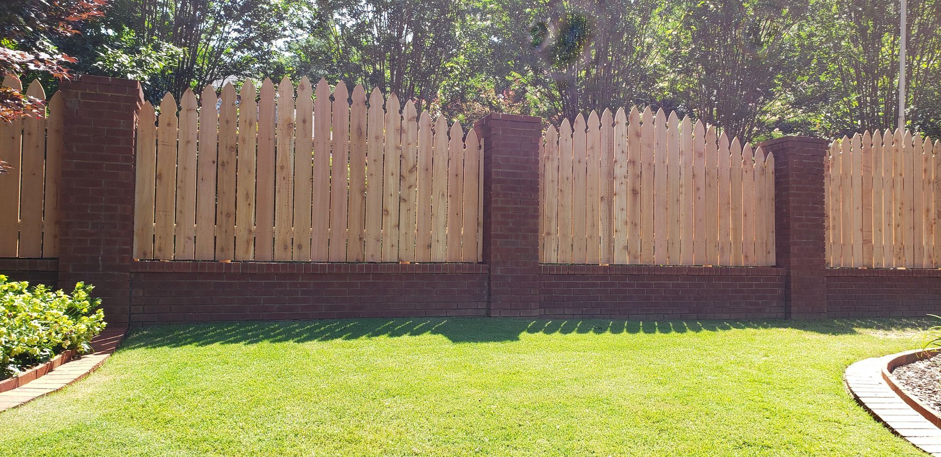 Wooden fence with brick columns and base in a yard with grass.