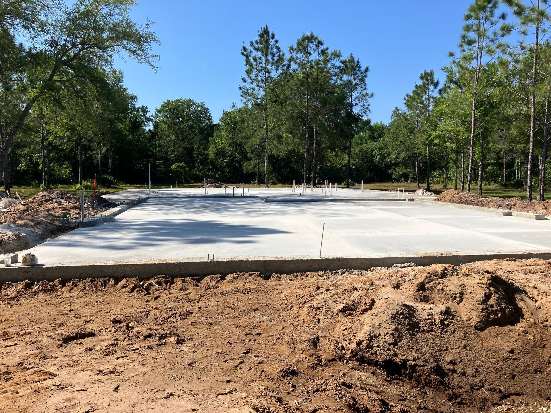 A concrete foundation is being built in a dirt field with trees in the background.