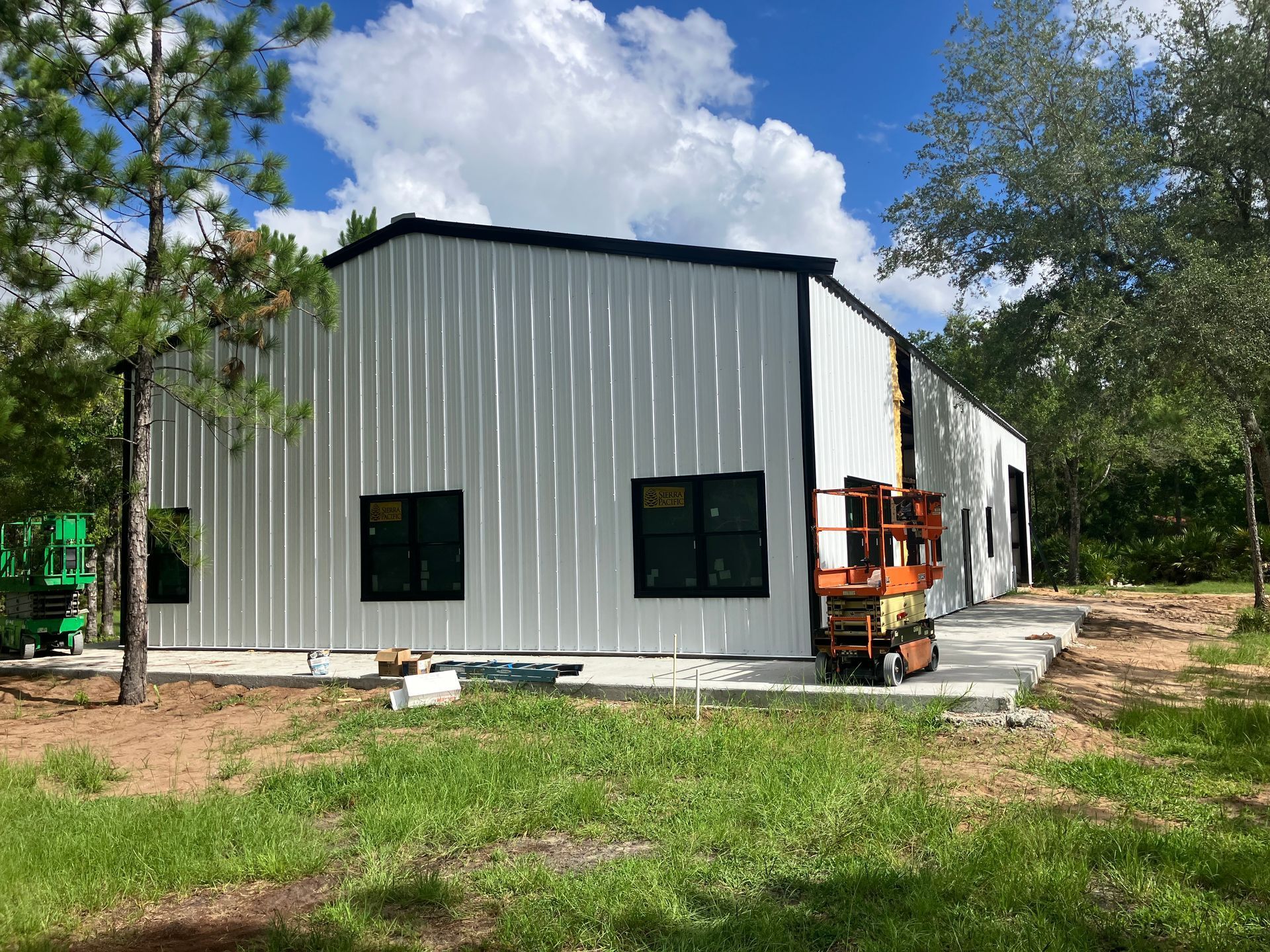 A large white metal building is being built in the middle of a grassy field.