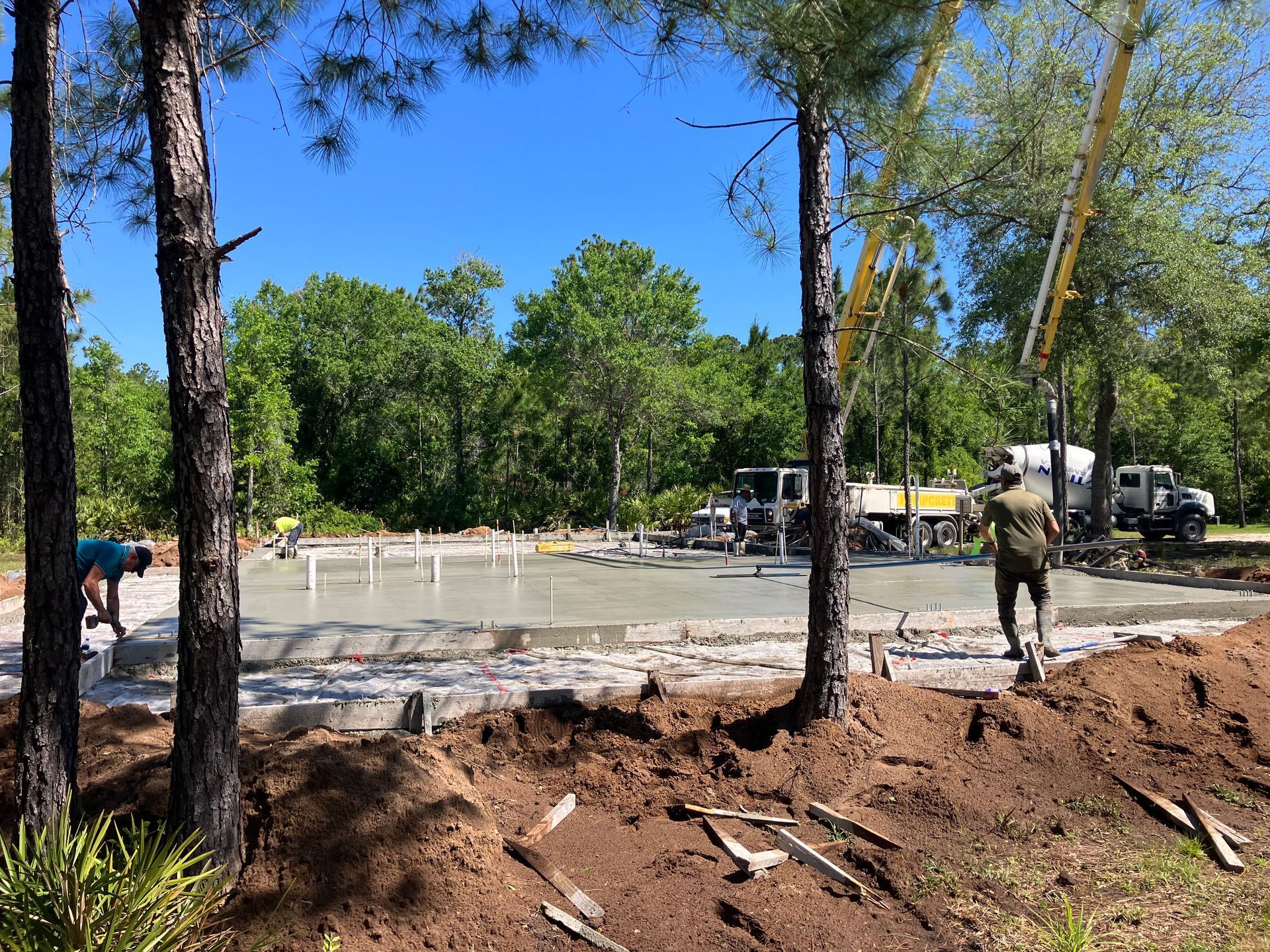 A construction site with a concrete pump in the background surrounded by trees.