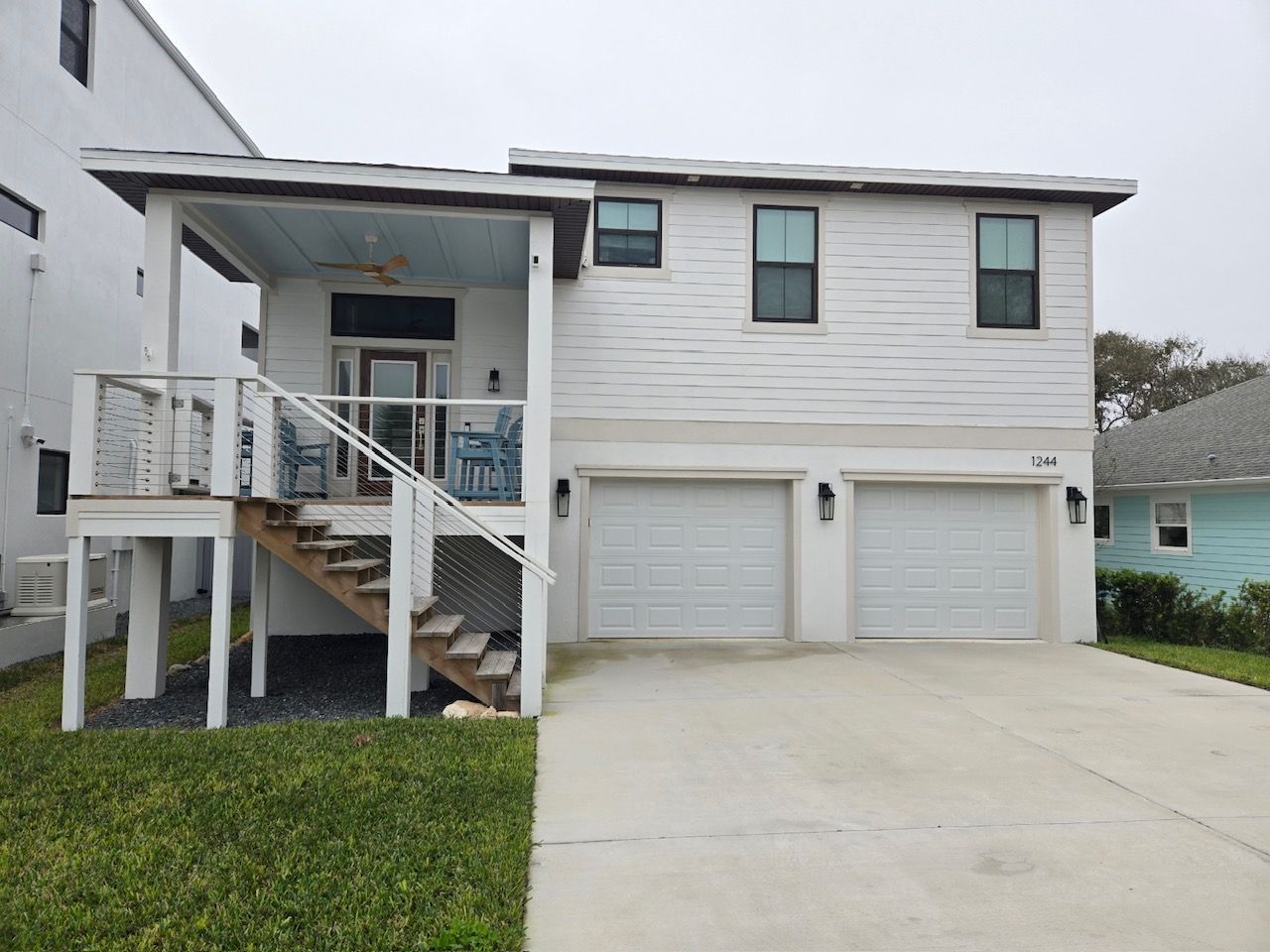 A white house with two garages and stairs leading up to the second floor.