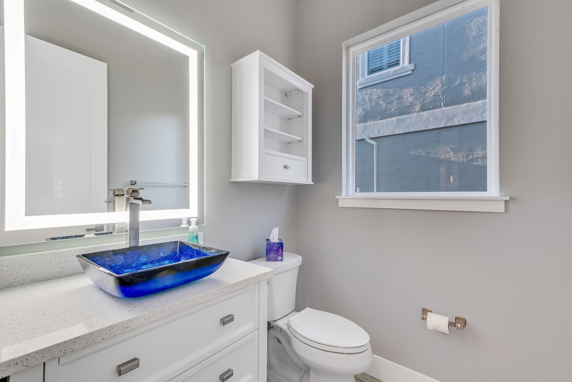 A bathroom with a toilet, sink, mirror and window.