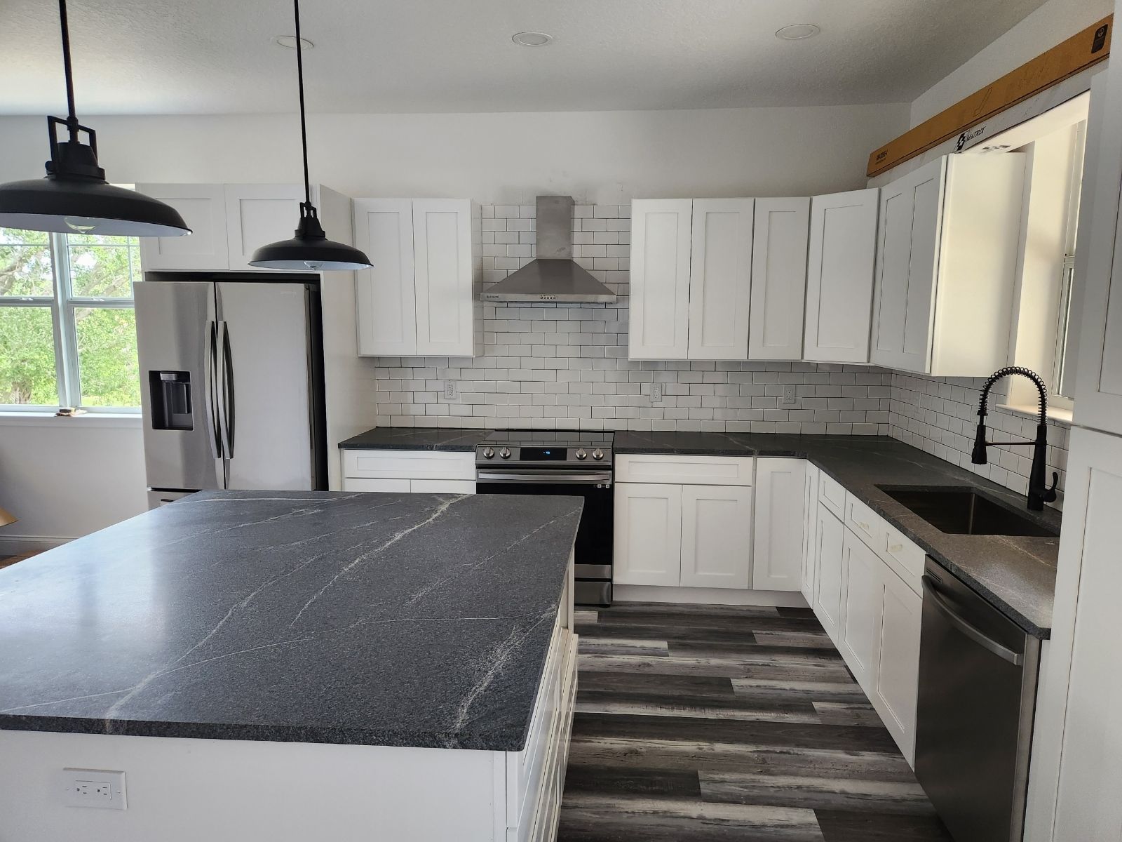 A kitchen with white cabinets, black counter tops, stainless steel appliances and a large island.