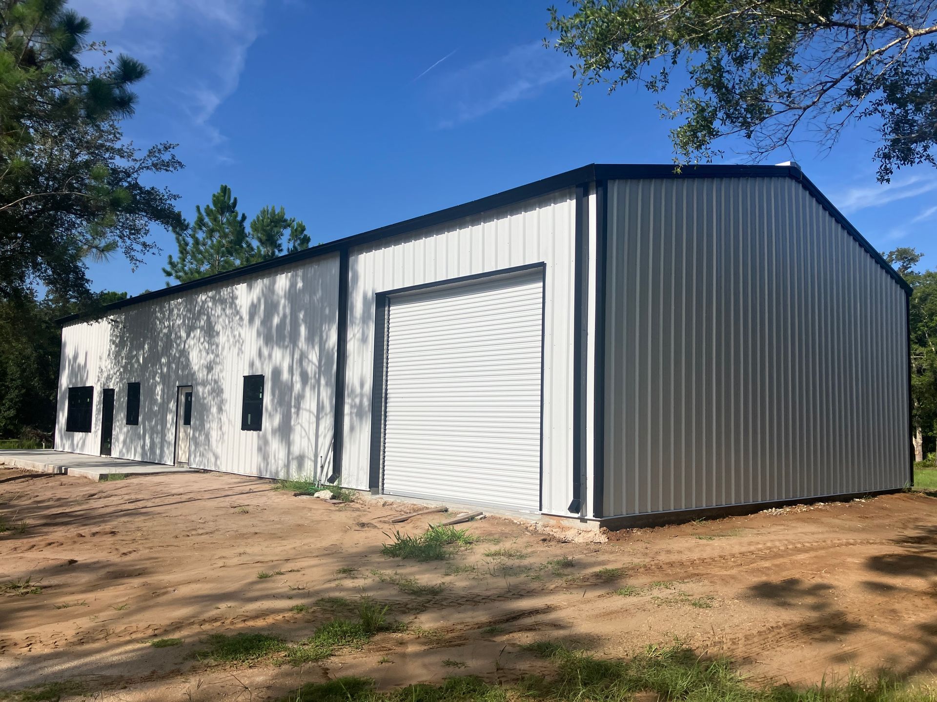 A large metal building with a garage door is sitting in the middle of a dirt field.