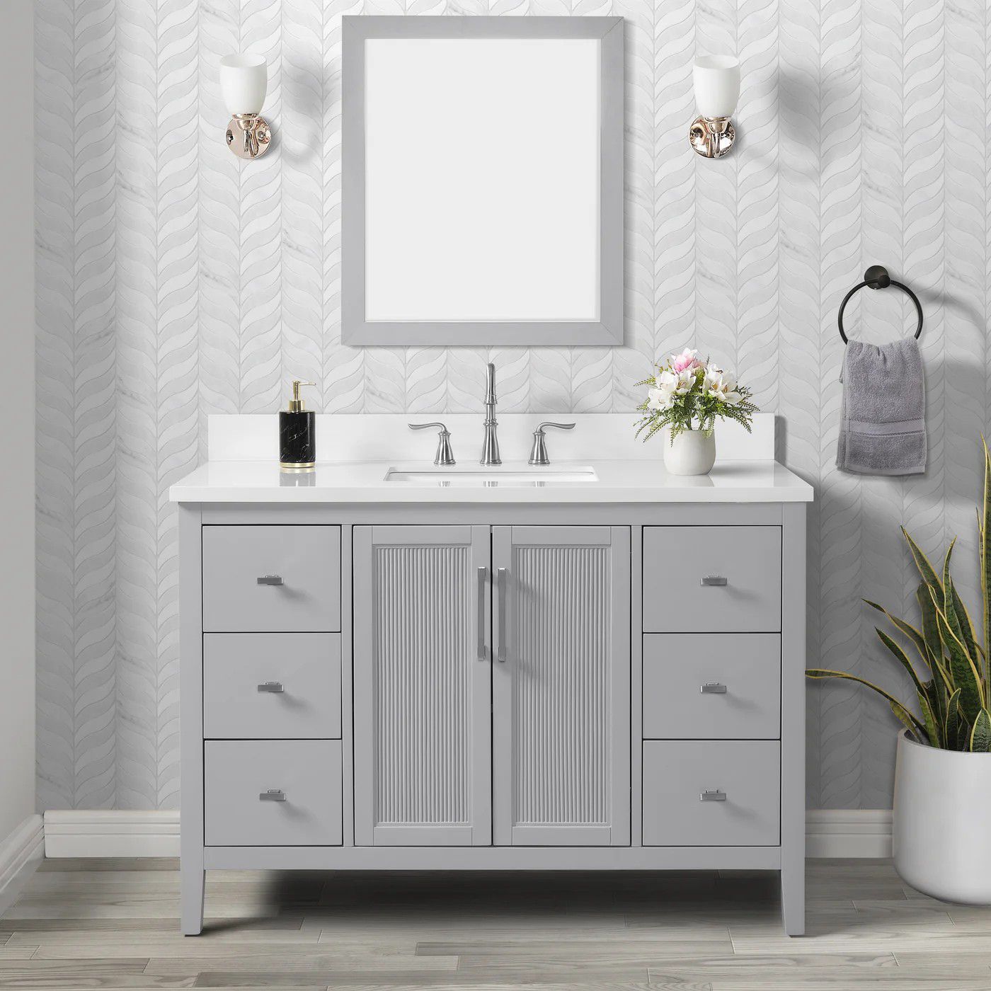 Gray bathroom vanity with mirror, sink, wall sconces, and decorative flowers in a light patterned room