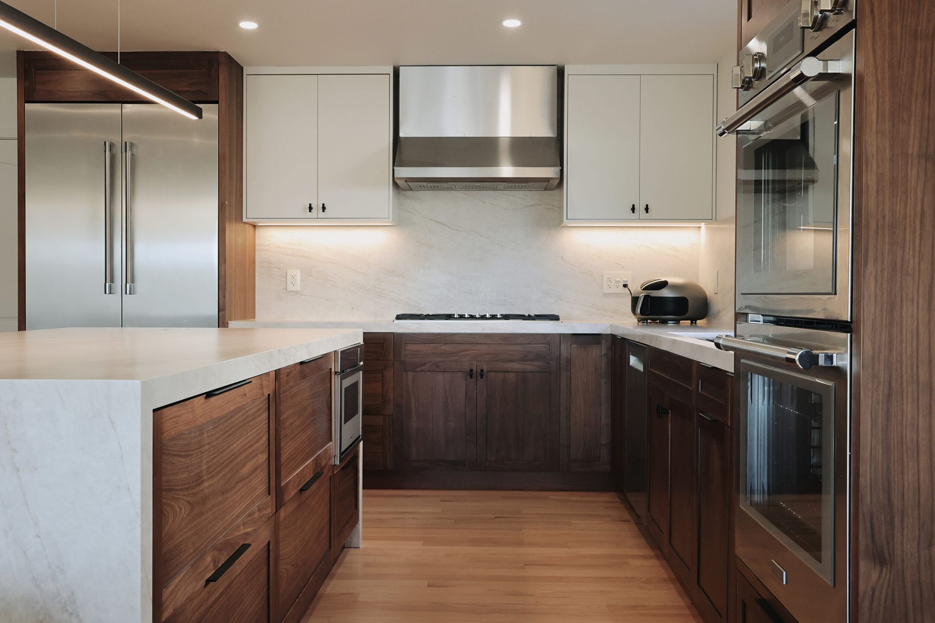 Modern kitchen with white cabinets, dark wood lower cabinets, stainless steel appliances, and wood flooring