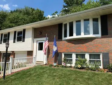A brick house with black shutters and a blue and white flag on the front lawn.
