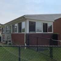 A brick house with a white roof and a lot of windows is behind a chain link fence.