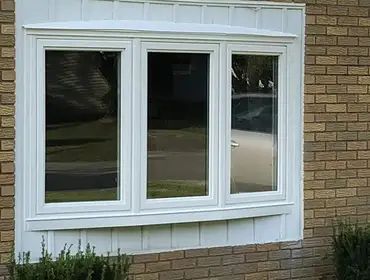 A white window is on the side of a brick building.