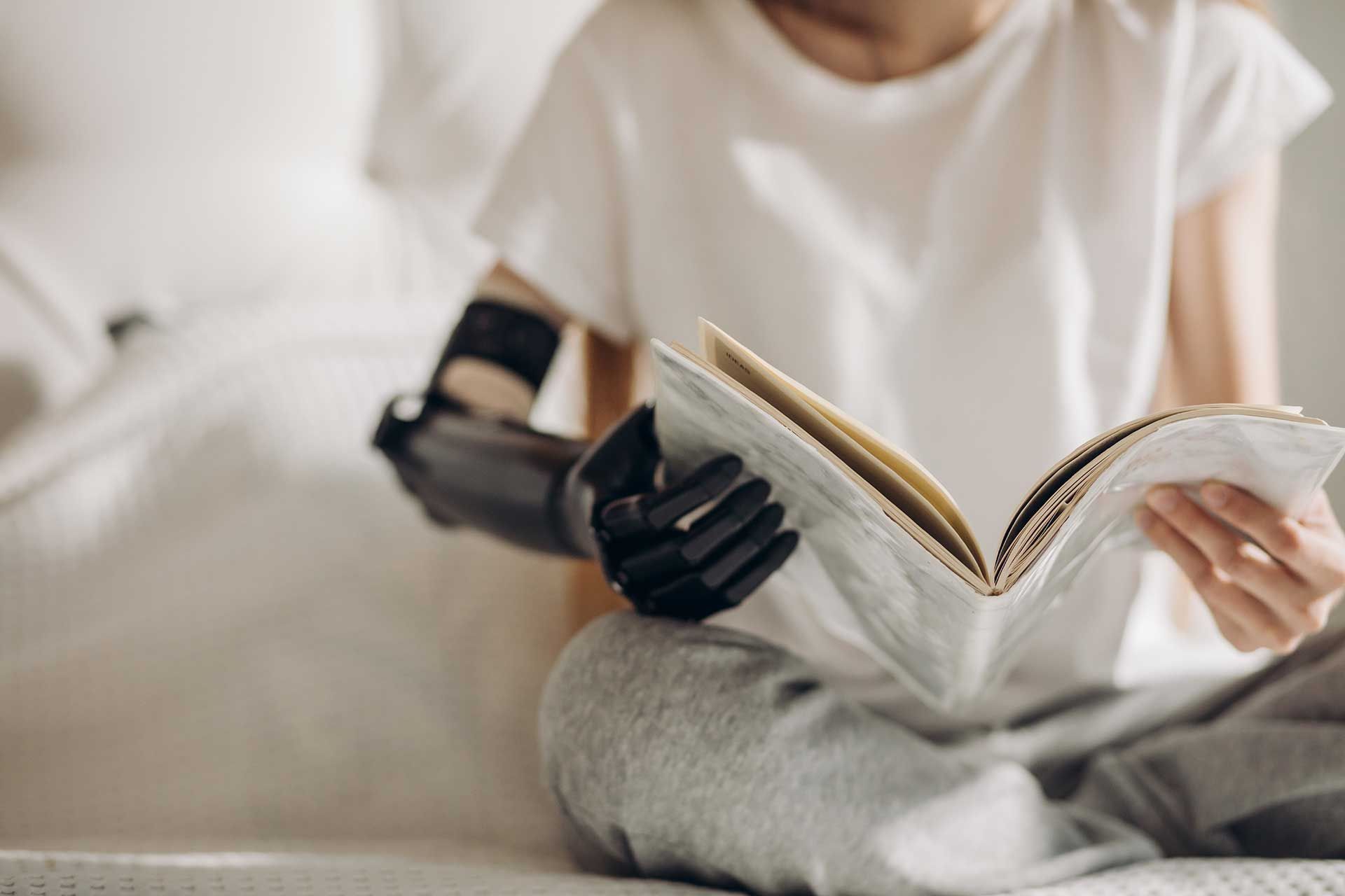 person with a prosthetic arm reading a book while sitting on a bed