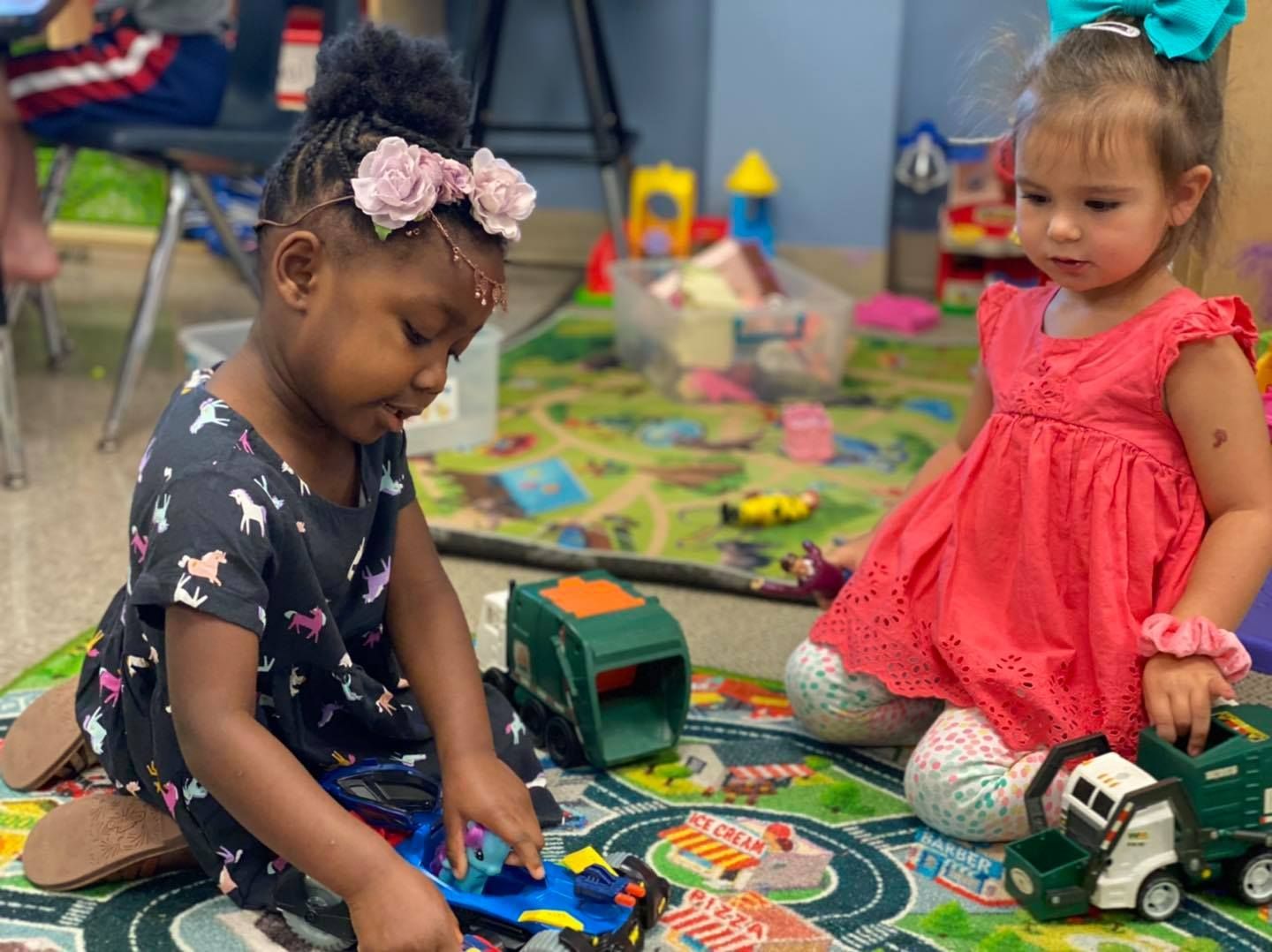 Children playing with toy trucks on a colorful rug in a classroom setting