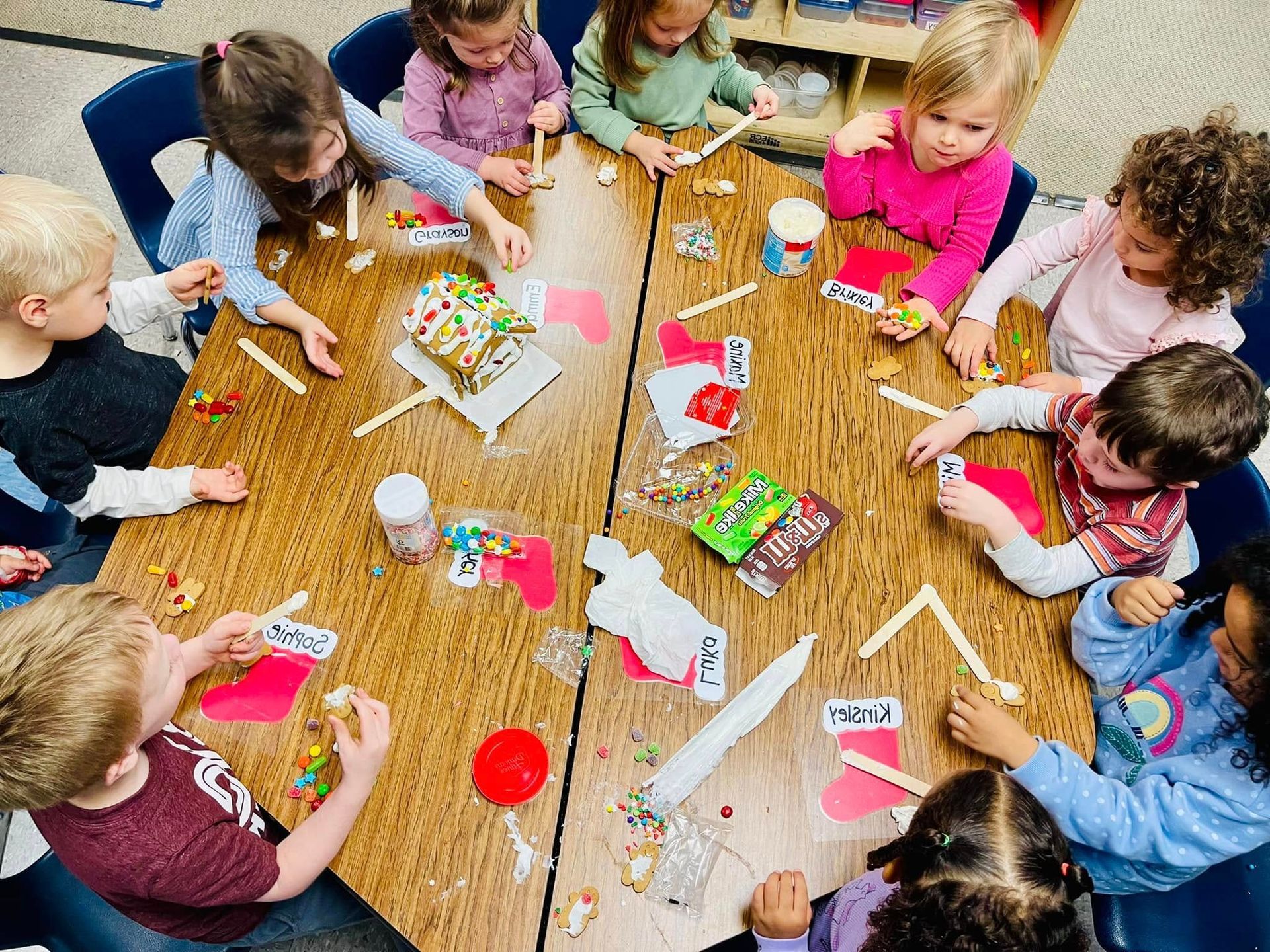 Children crafting around a table with colored paper, glue, and markers in a classroom setting