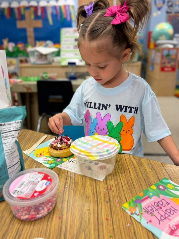 Child decorating a cupcake at a classroom table with colorful snacks and containers nearby