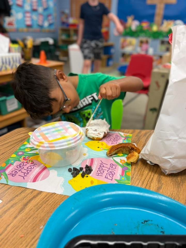 Child leaning over a table with colorful plates, food samples, and a blue basin in a shop or market setting