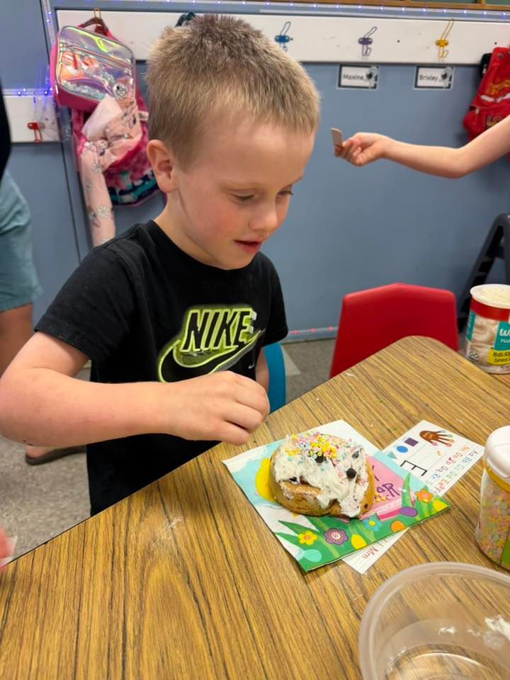 Child at a classroom table decorating a sprinkled treat on colorful paper.