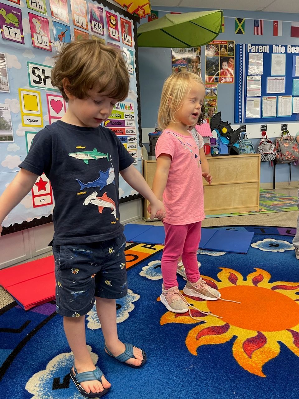 Two children standing on a colorful classroom rug with a sun design
