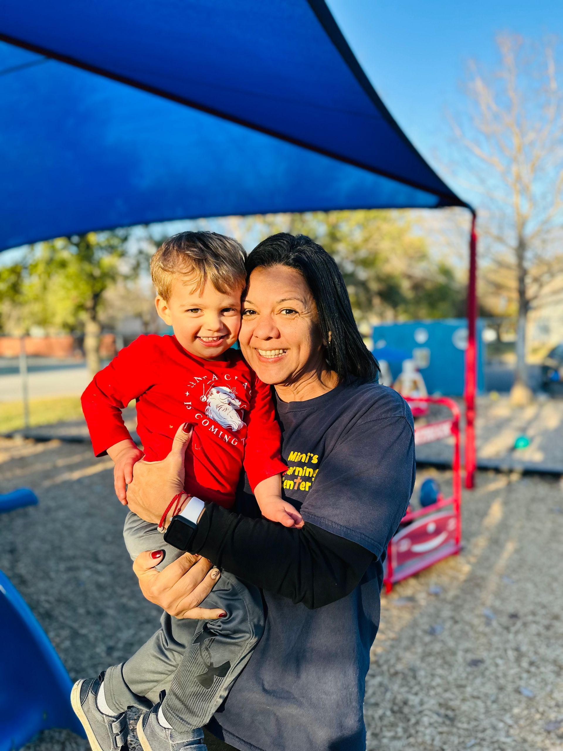 Adult holding a smiling child under a blue canopy at an outdoor playground