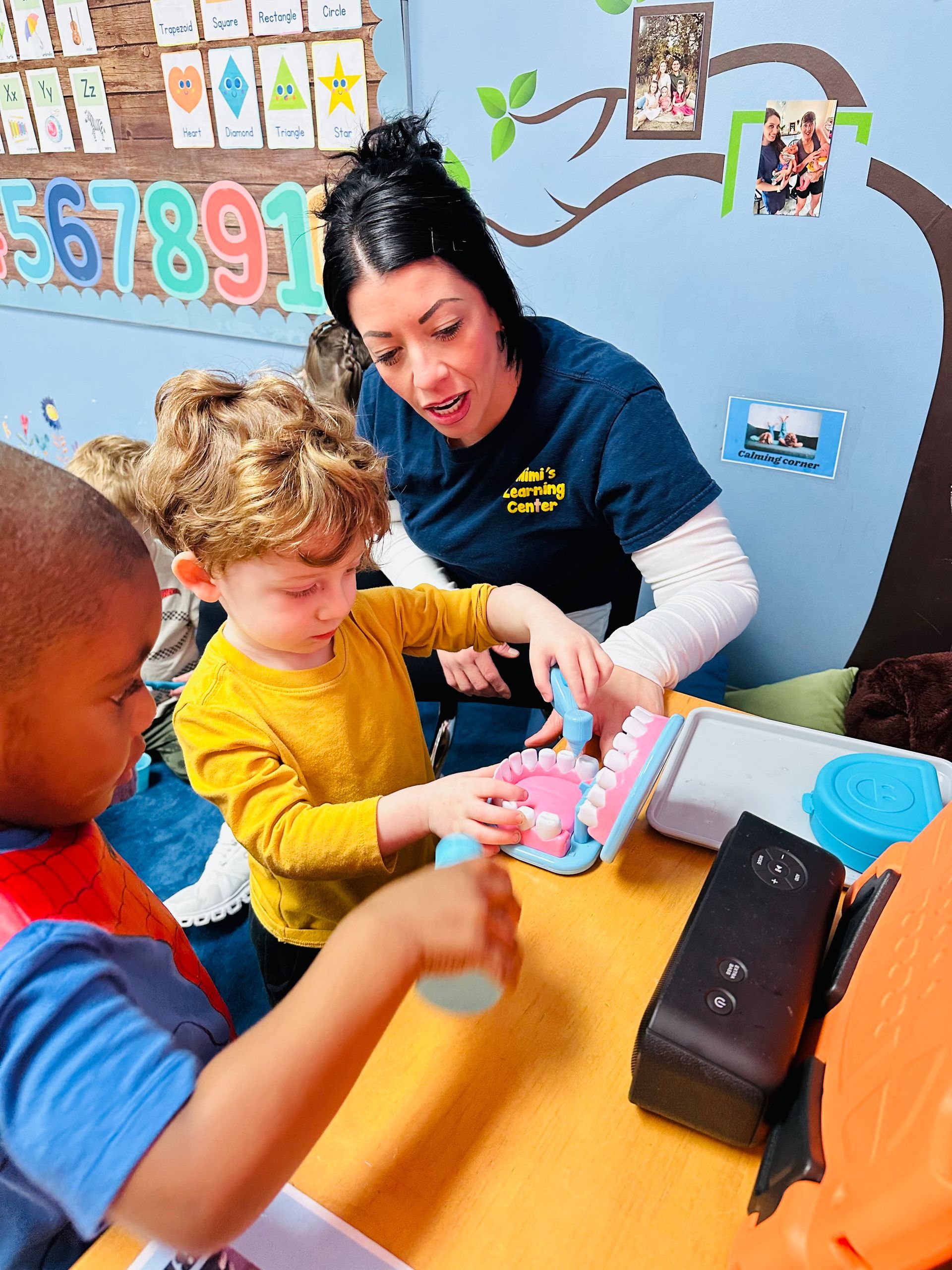 Teacher helping children with a craft activity at a colorful classroom table