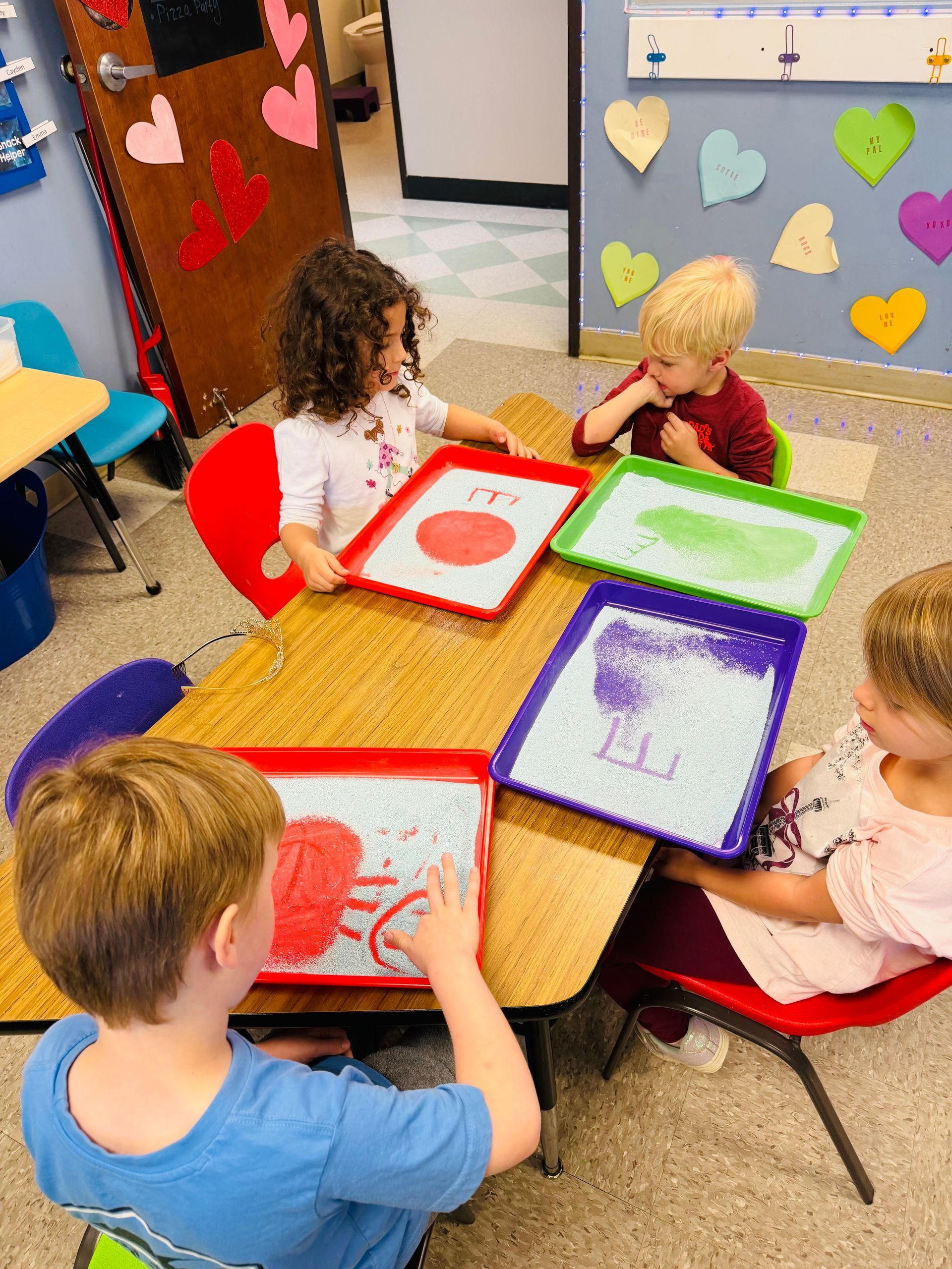 Children painting at a table with colorful art trays in a classroom.