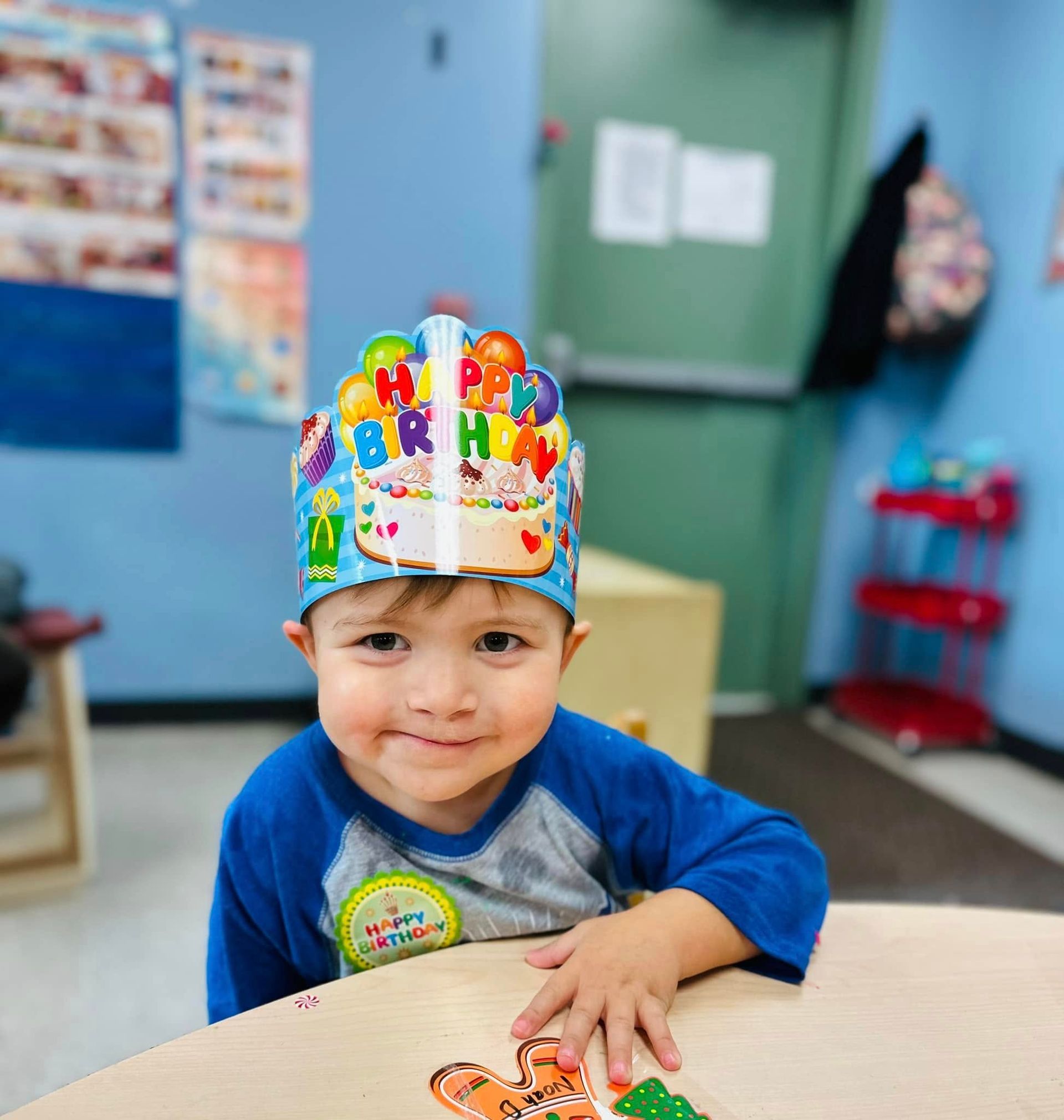 Smiling child wearing a colorful birthday crown at a classroom table