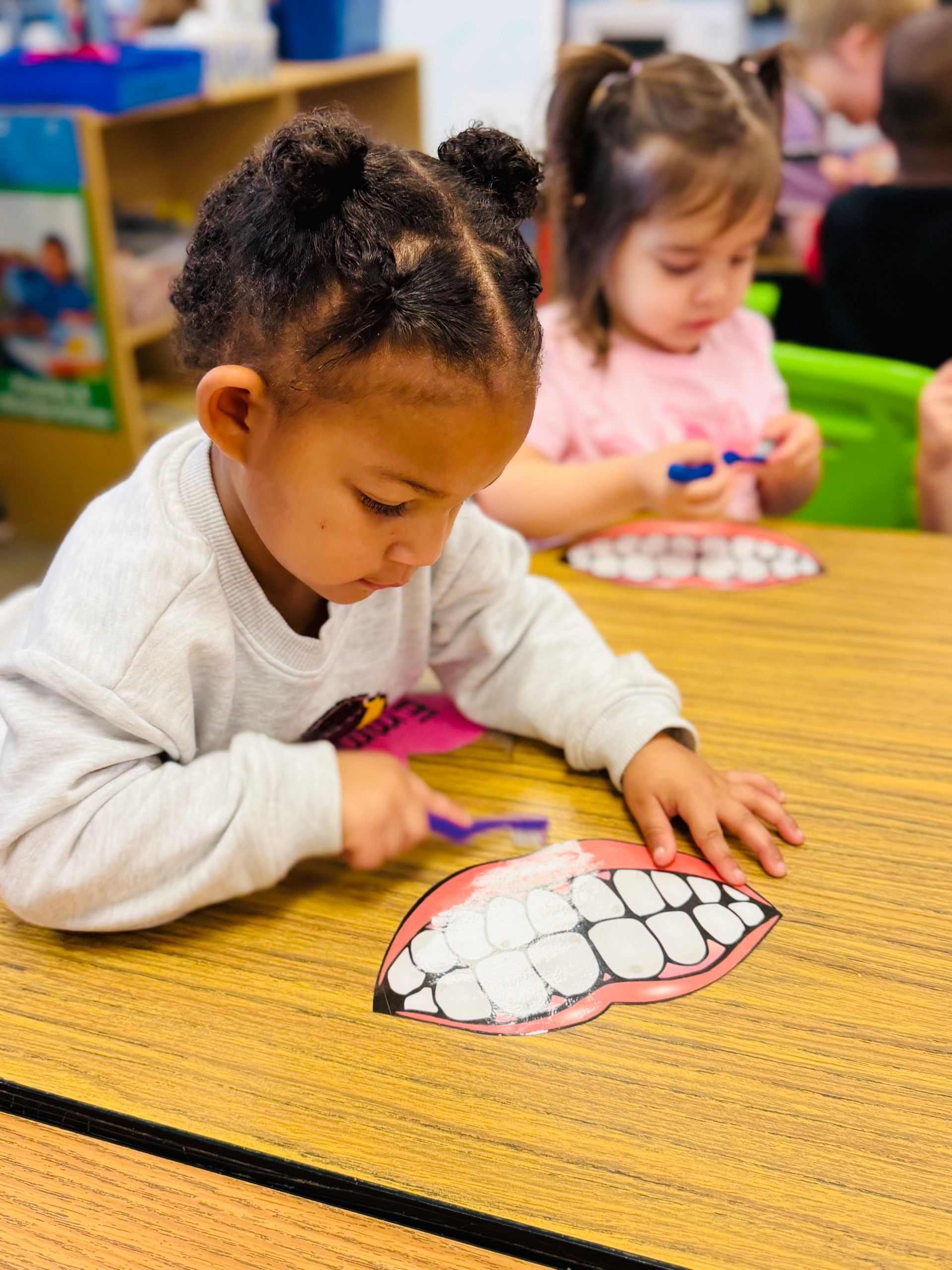 Child coloring a fish worksheet at a classroom table while another child works in the background