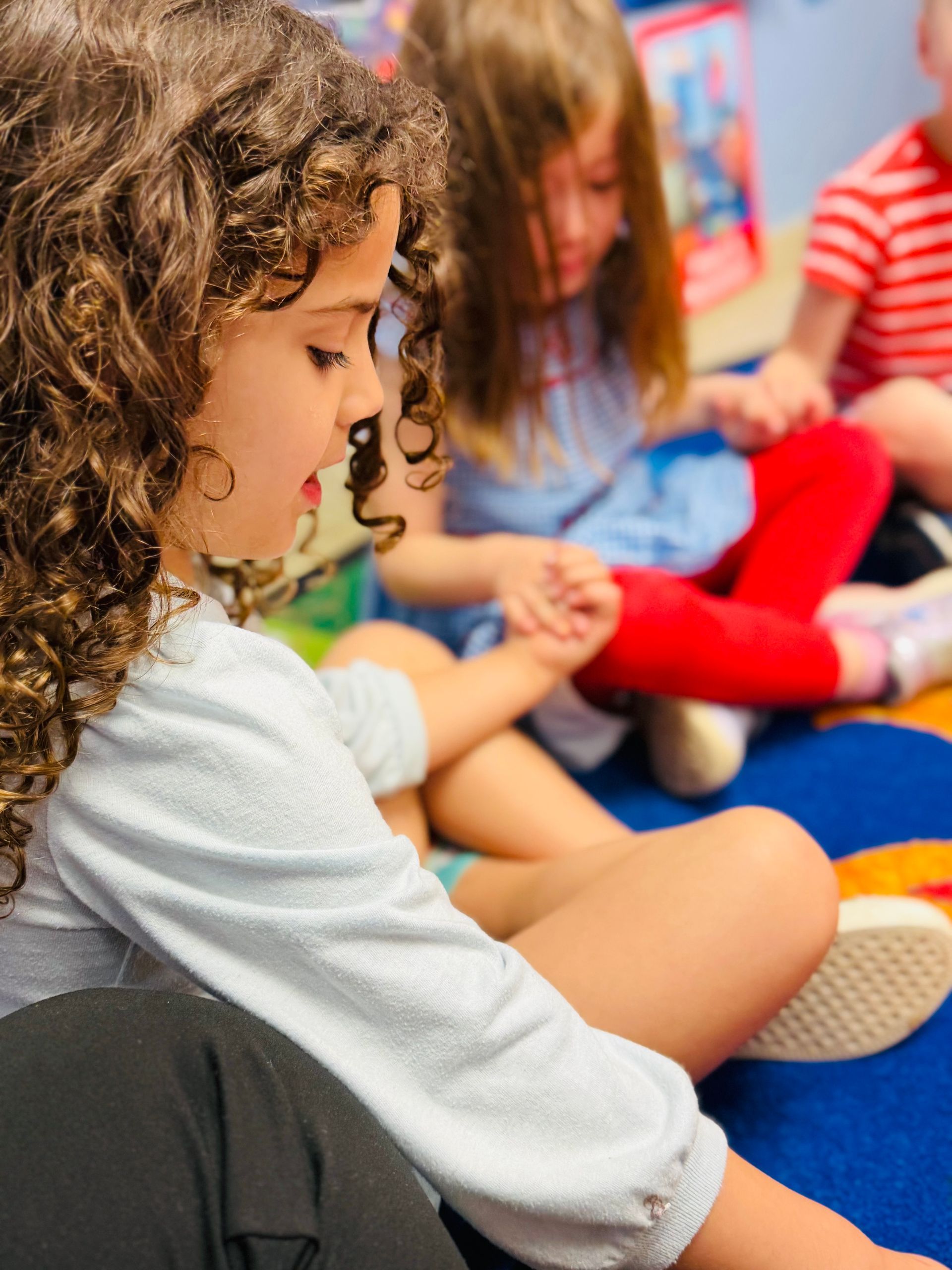 Children sitting on a blue carpet, focused on an activity together in a classroom.