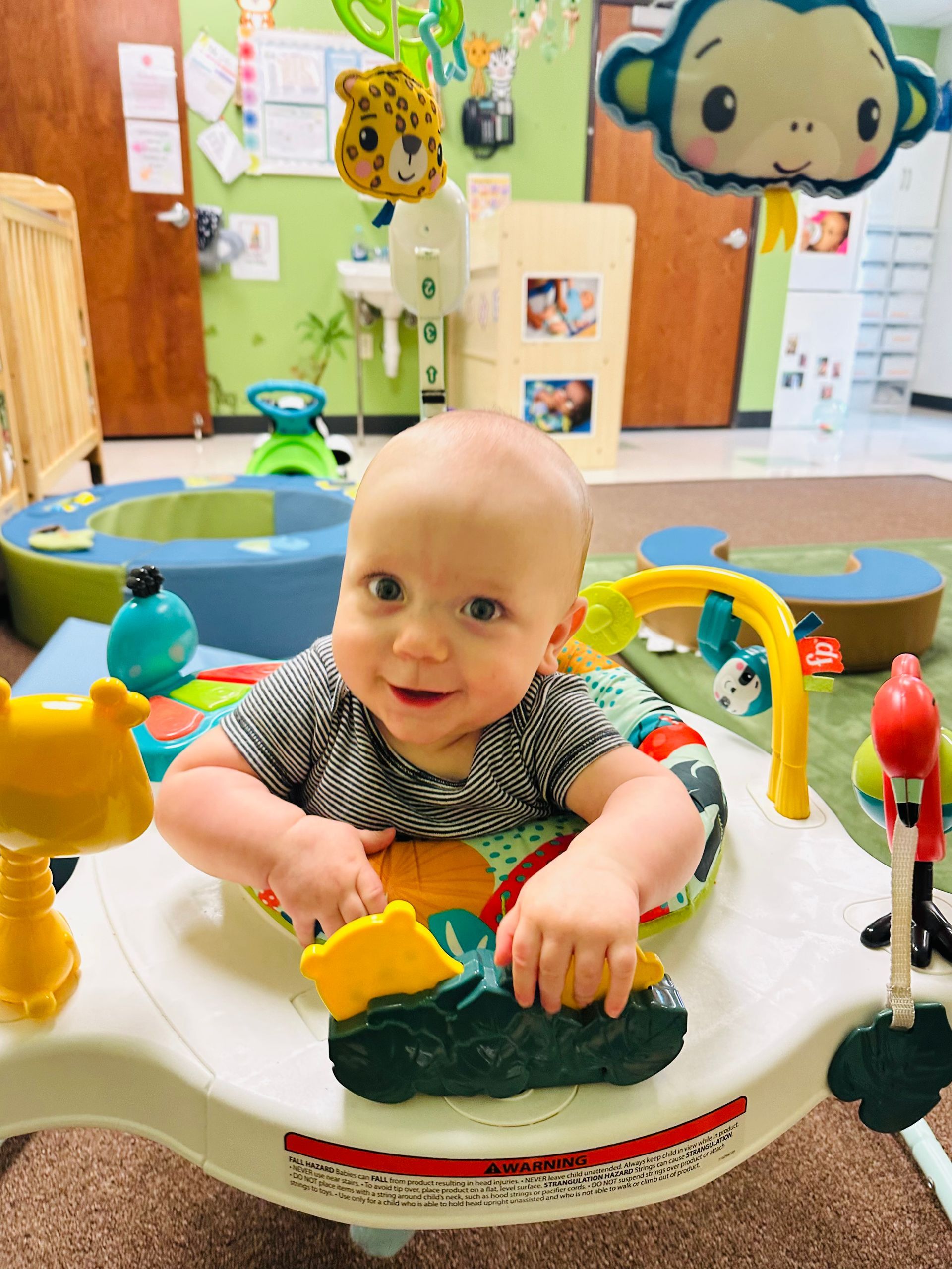 Smiling baby in a green toy seat at a colorful indoor play area