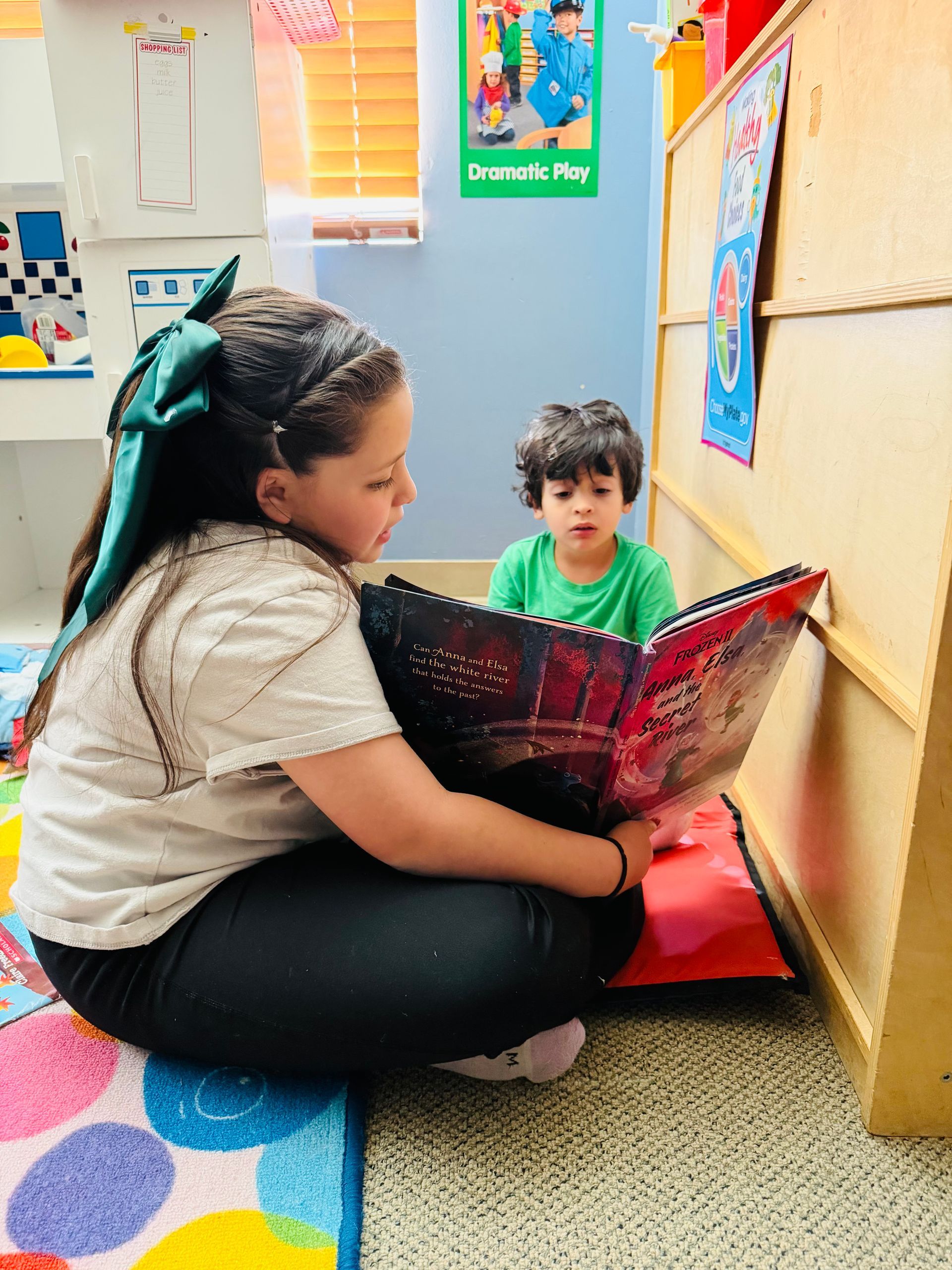 Teacher reading a book to a child in a colorful classroom corner
