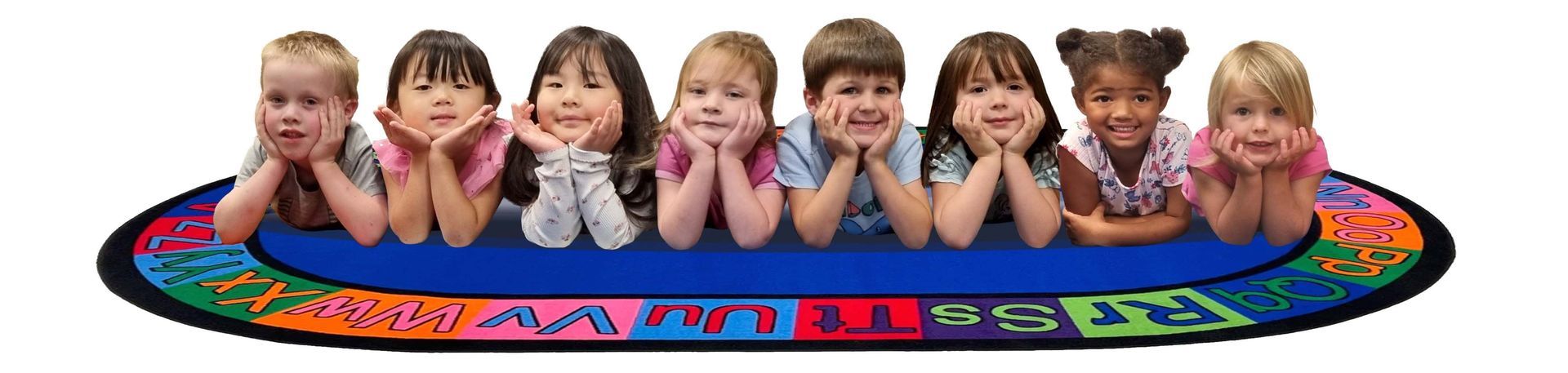 Seven children posing behind a colorful oval play table with letters and numbers on a white background