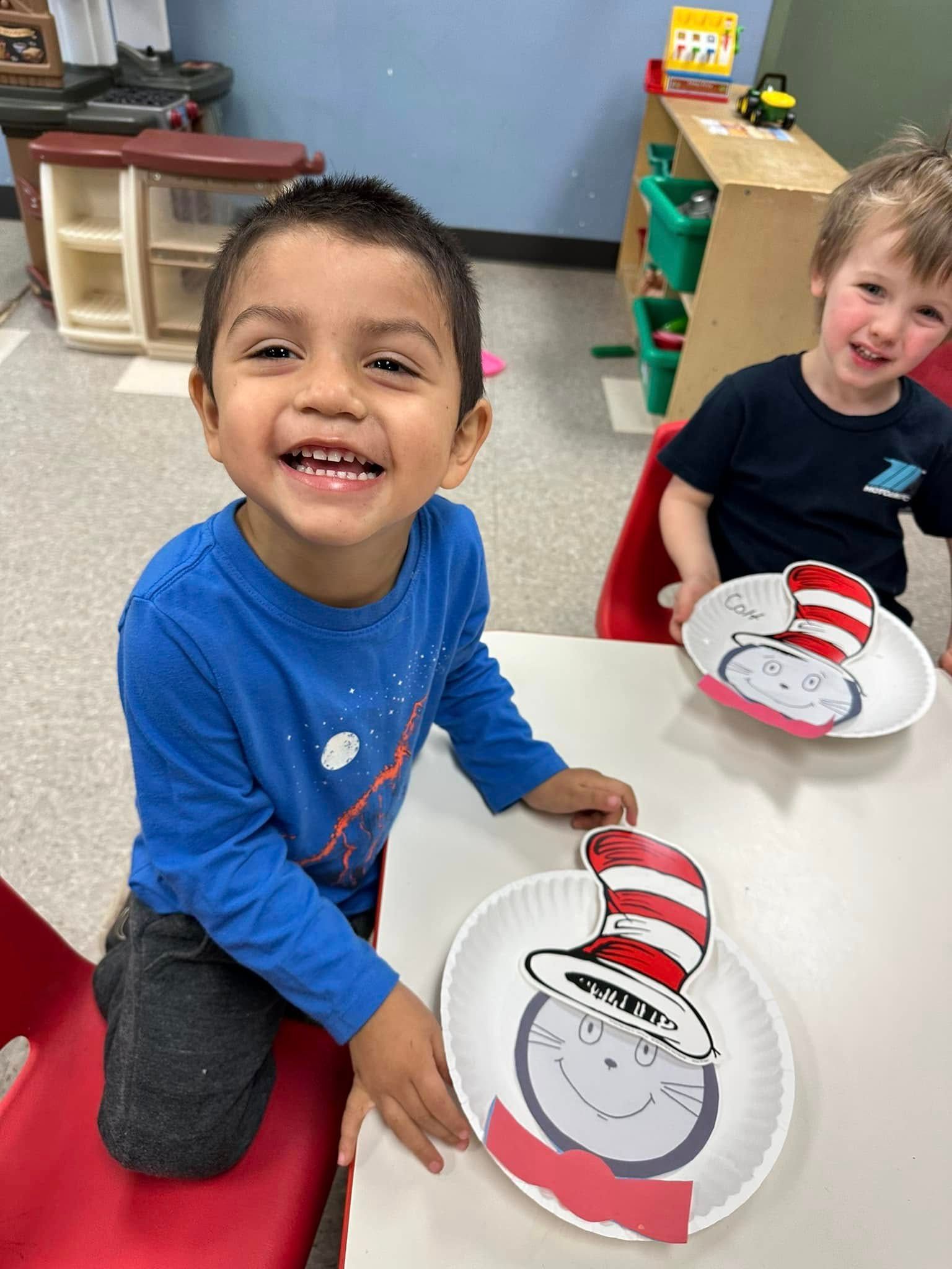 Two children smiling and holding red-and-white paper crafts in a classroom.