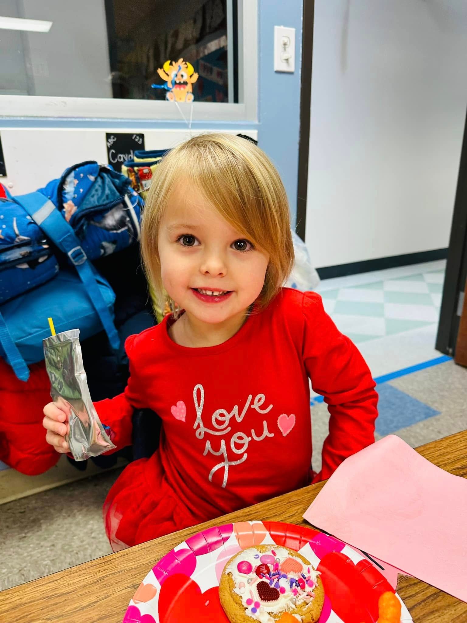 Child in a red shirt smiling at a table with a decorated donut and a small snack bag.