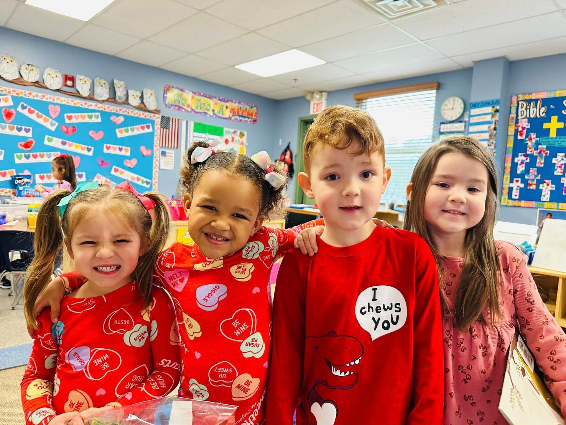 Four children in red shirts smiling in a decorated classroom