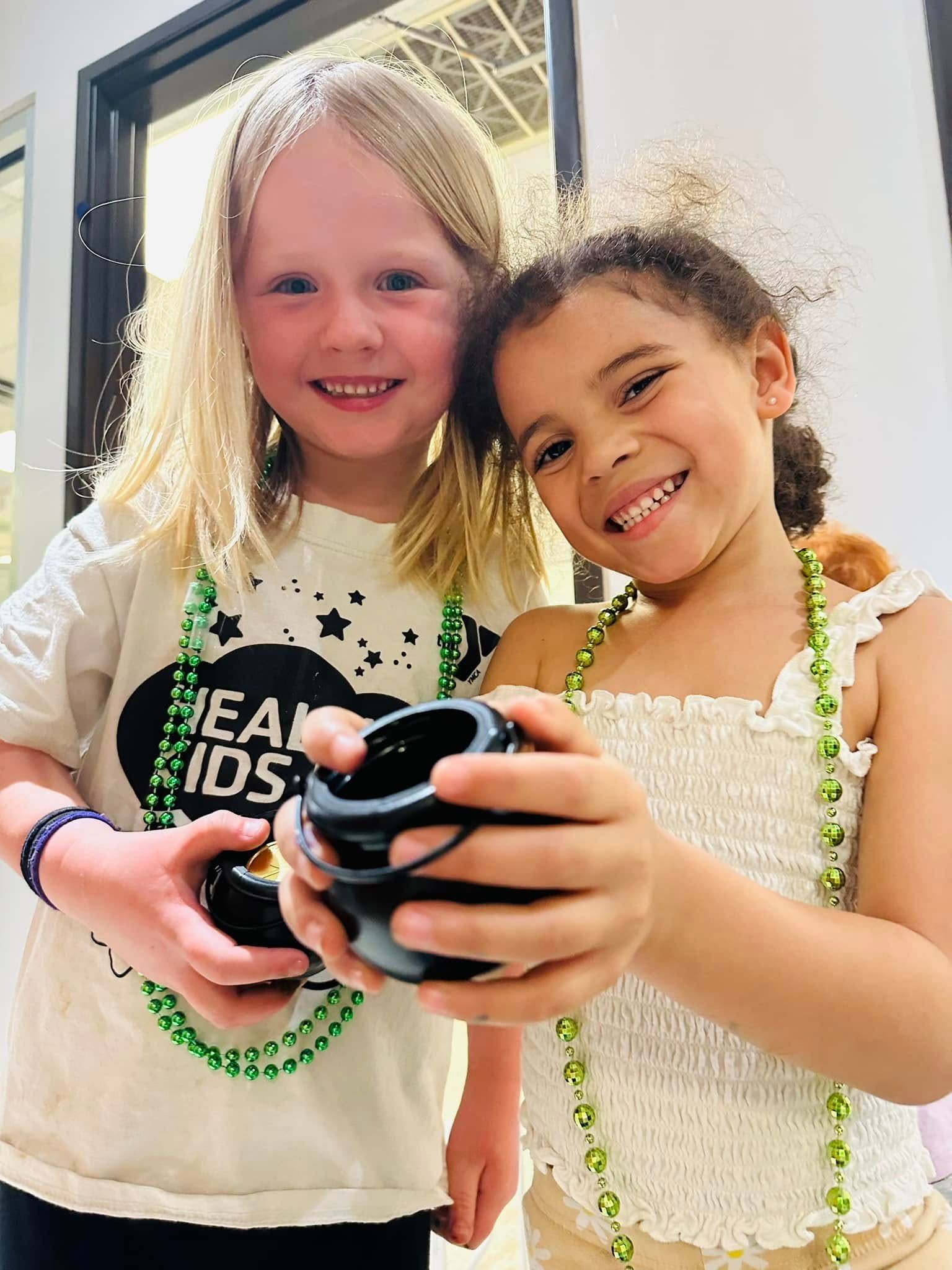 Two smiling children holding a black camera outdoors in bright sunlight