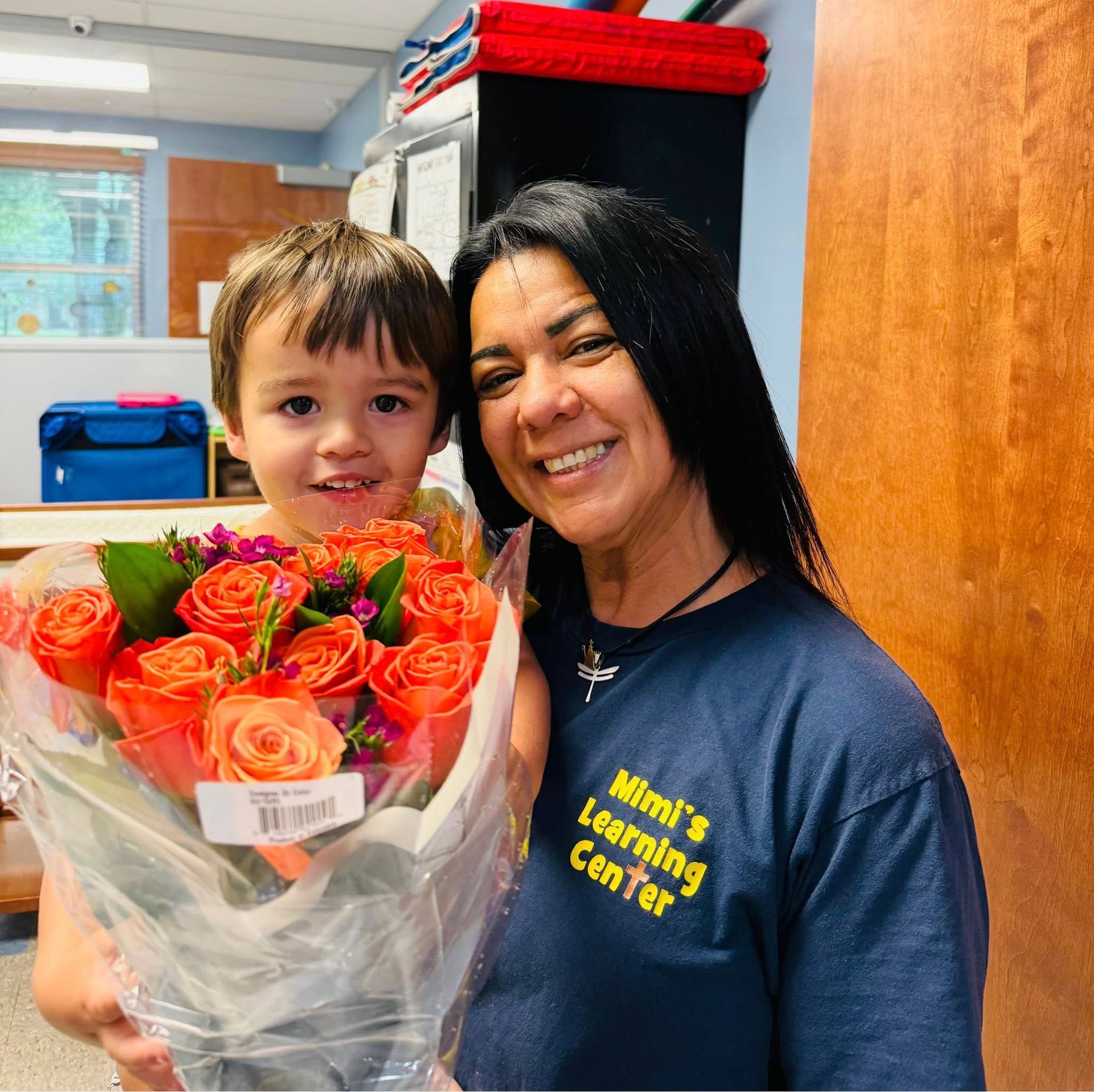 Smiling child holding orange roses with a woman in a learning center office