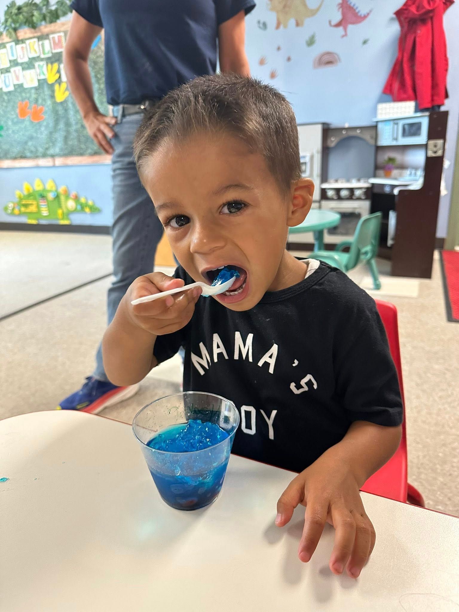 Toddler eating blue shaved ice at a table in a colorful room