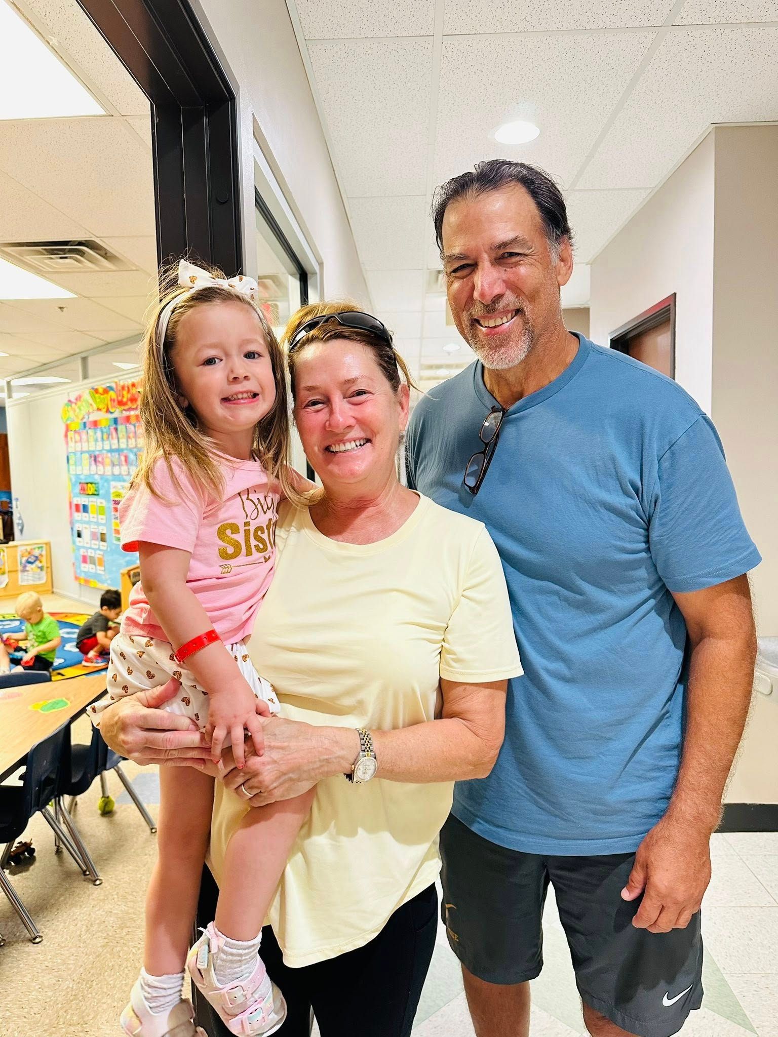 Three people smiling in a hallway, with one child being held by two adults.