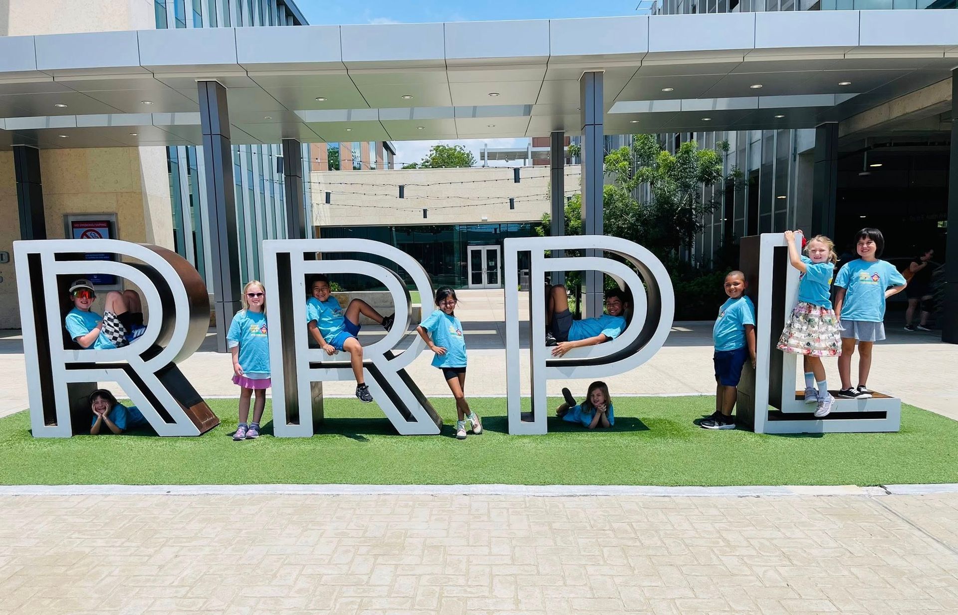People posing in front of large RRRR letters outside a modern building